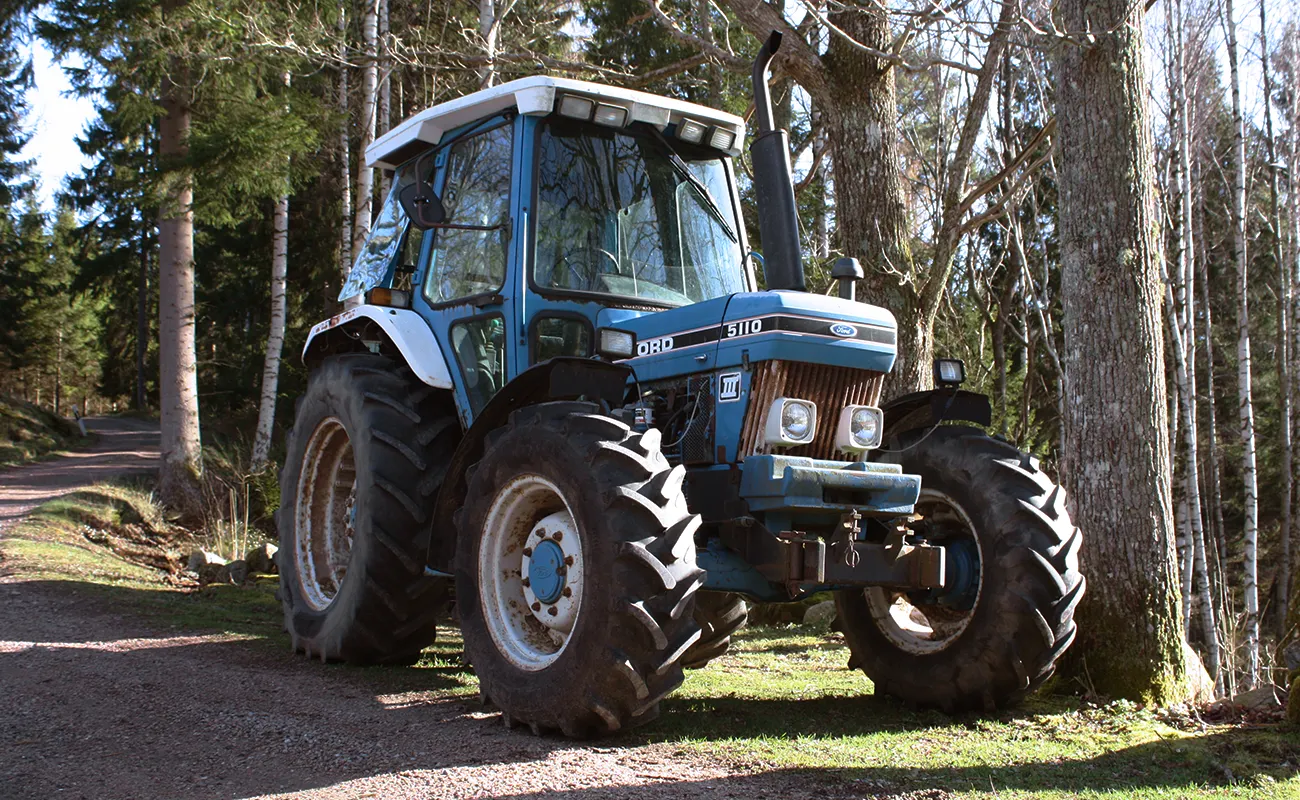 En Ford-traktor st&aring;r parkert p&aring; en grusvei i en skog.