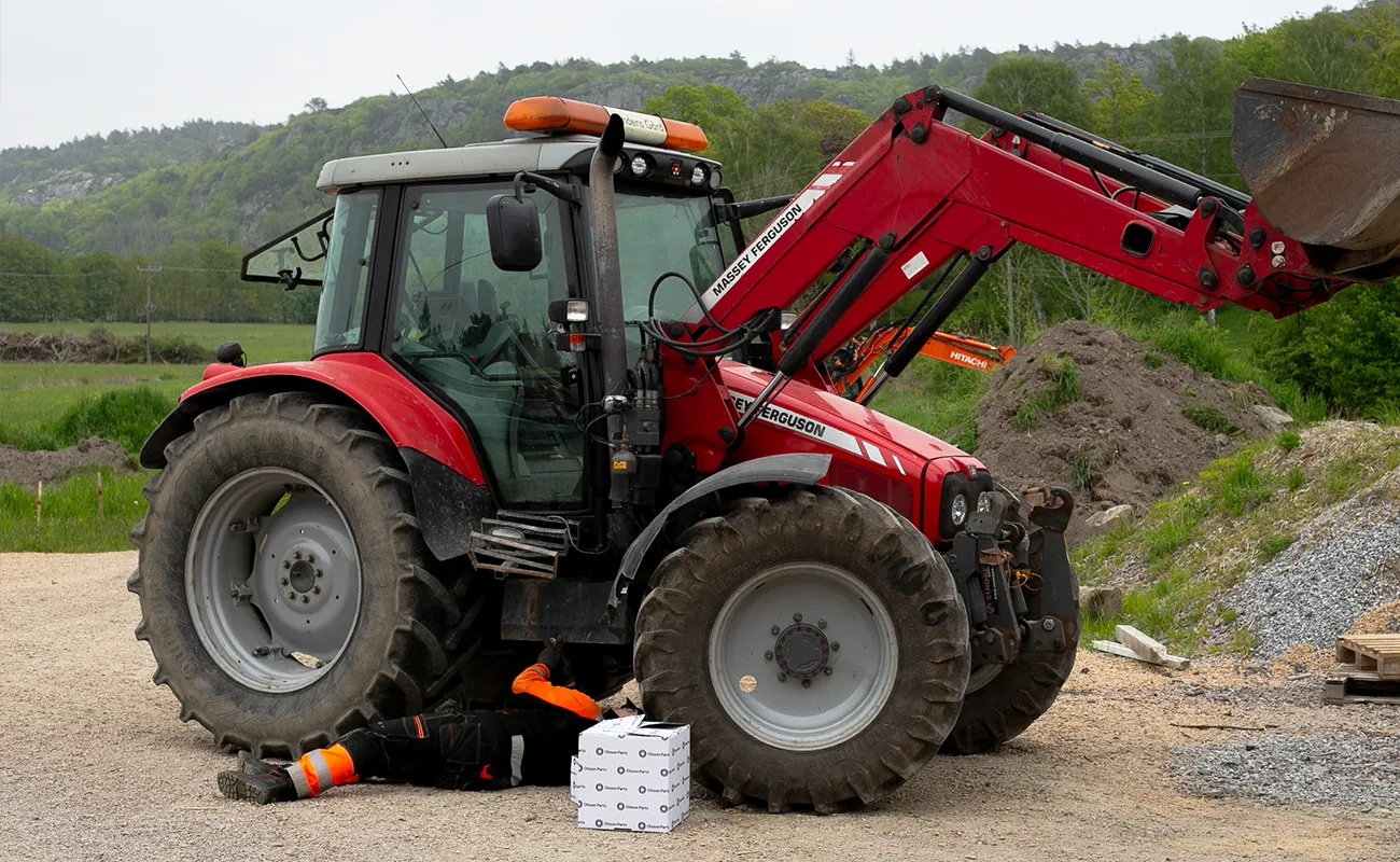 En person mekker p&aring; en Massey Ferguson-traktor.
