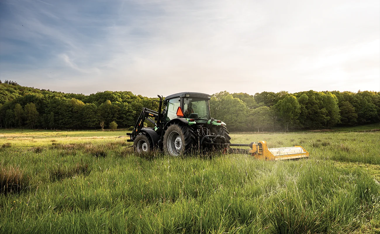 En Deutz-traktor st&aring;r parkerad p&aring; ett f&auml;lt framf&ouml;r en skog.
