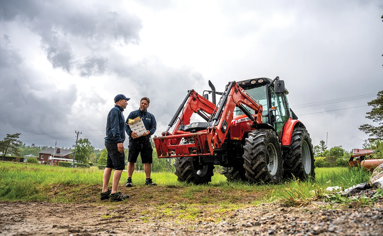Två personer står bredvid en Massey Ferguson-traktor. En person håller i en Olsson Parts låda.