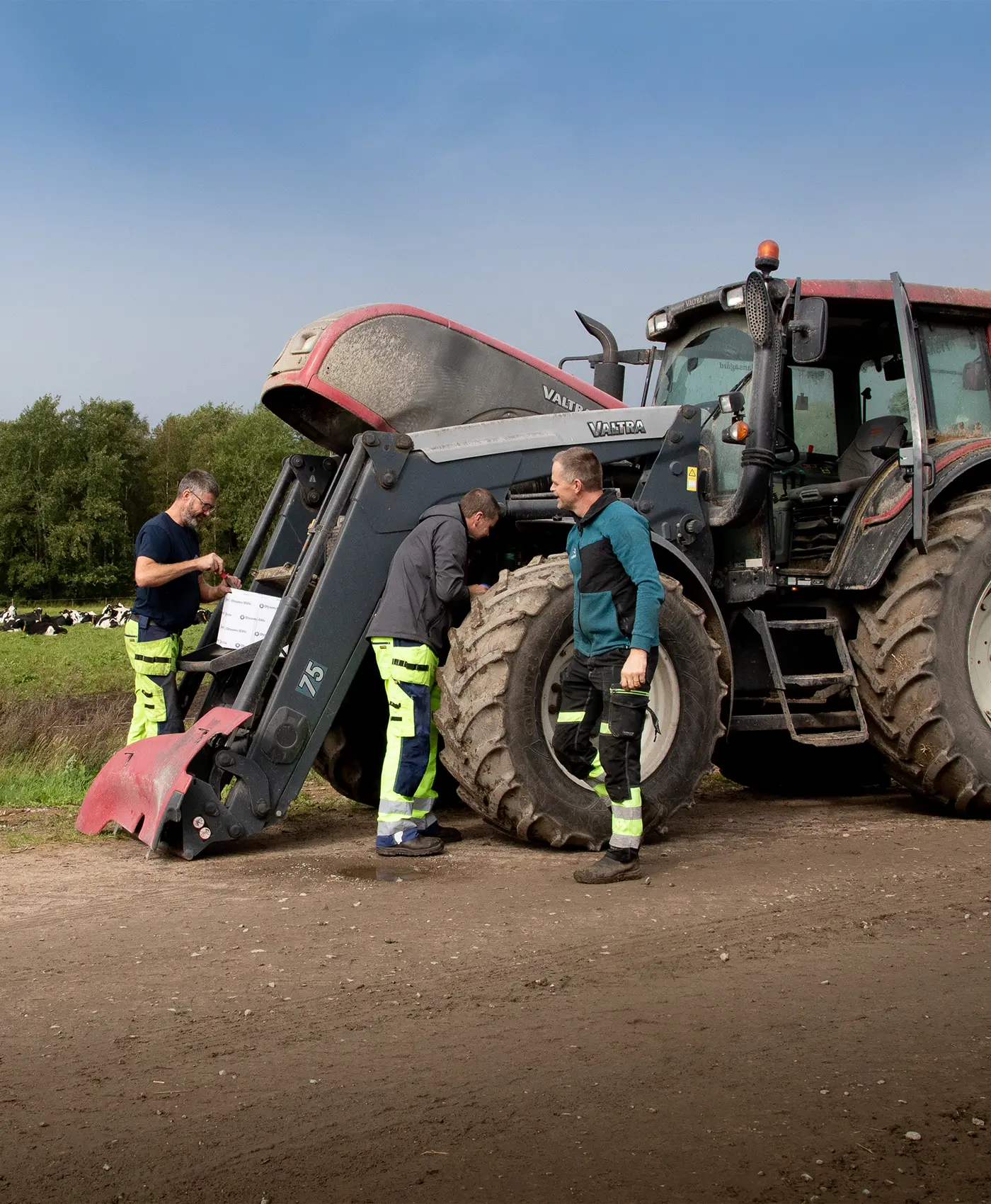 Tre personer arbetar på en Valtra-traktor med motorhuven uppfälld.