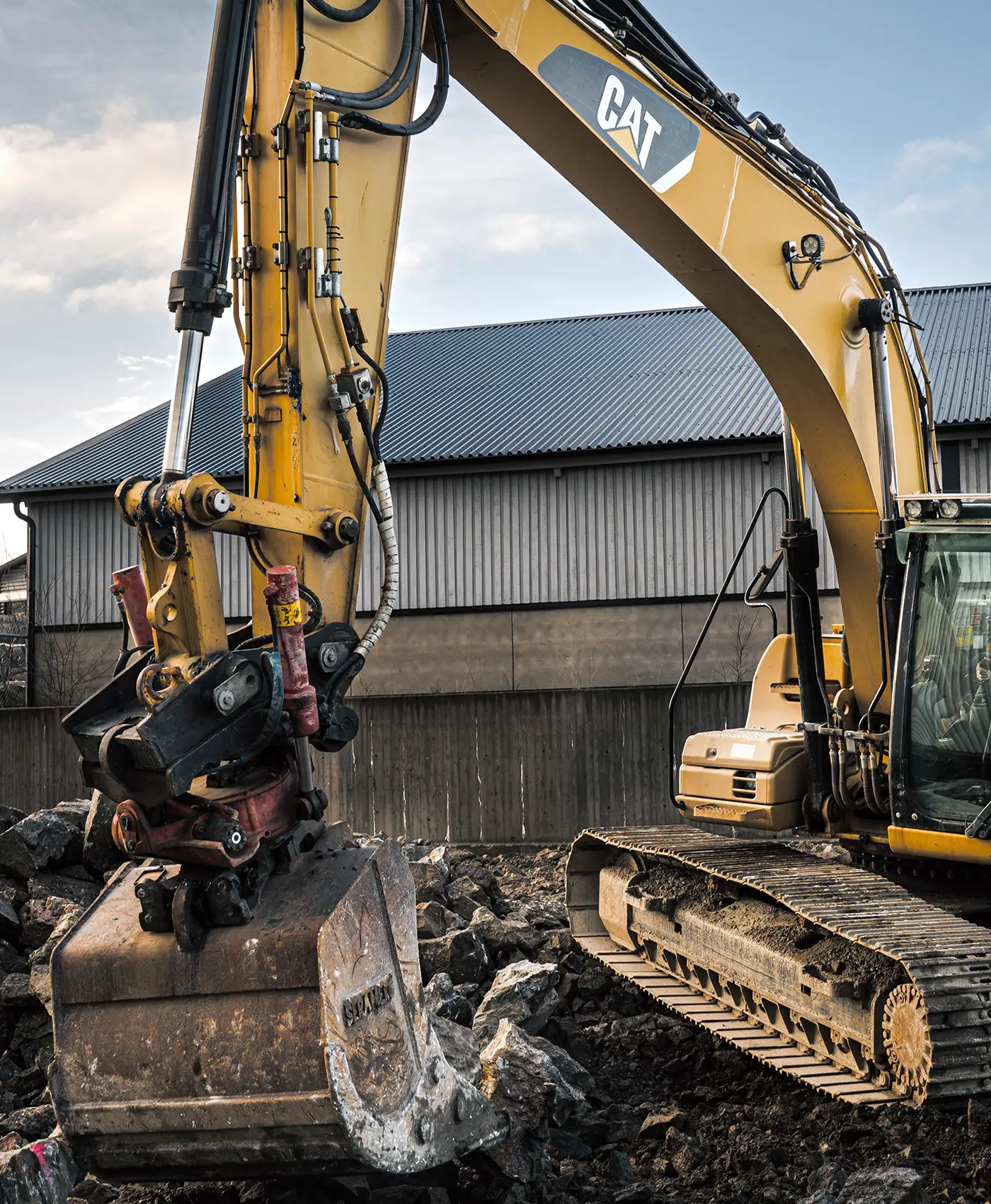En Caterpillar gravemaskine i arbejde foran et hus.