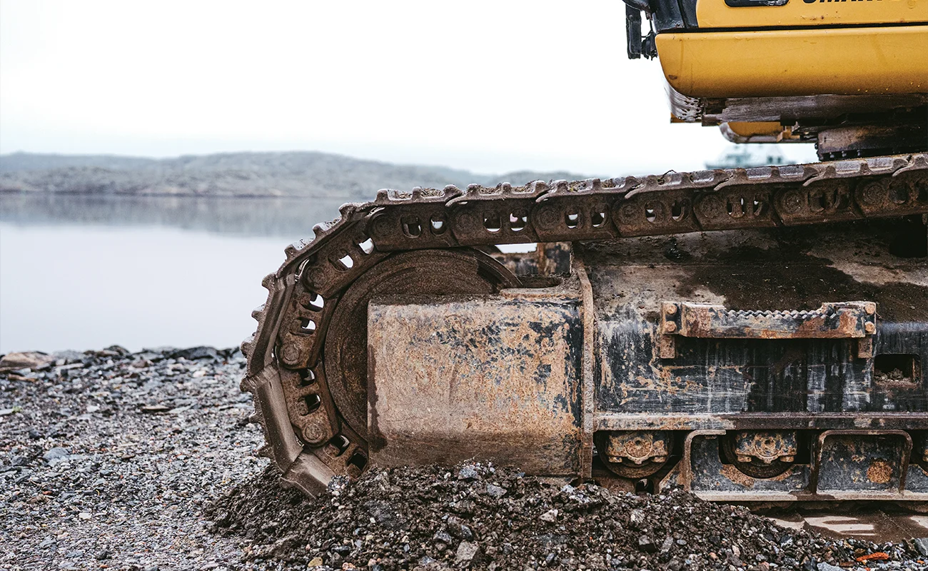 N&aelig;rbillede af larveb&aring;ndene p&aring; en Caterpillar gravemaskine med havet i baggrunden.
