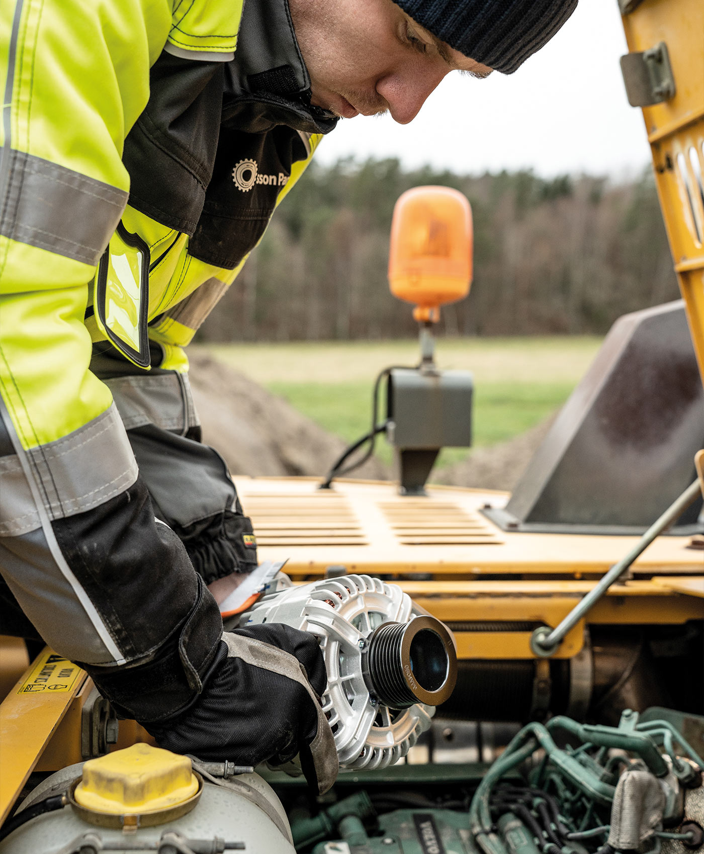 A person is installing an alternator in a Volvo excavator.