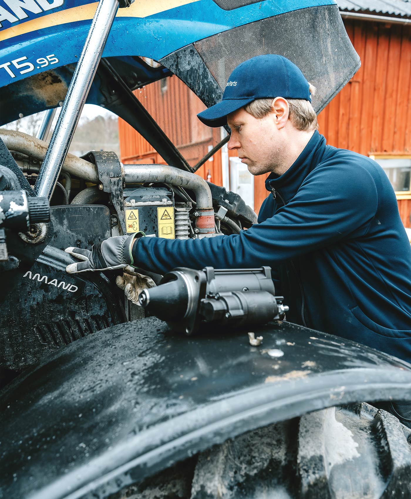 A person is working on a tractor with a starter motor next to them.