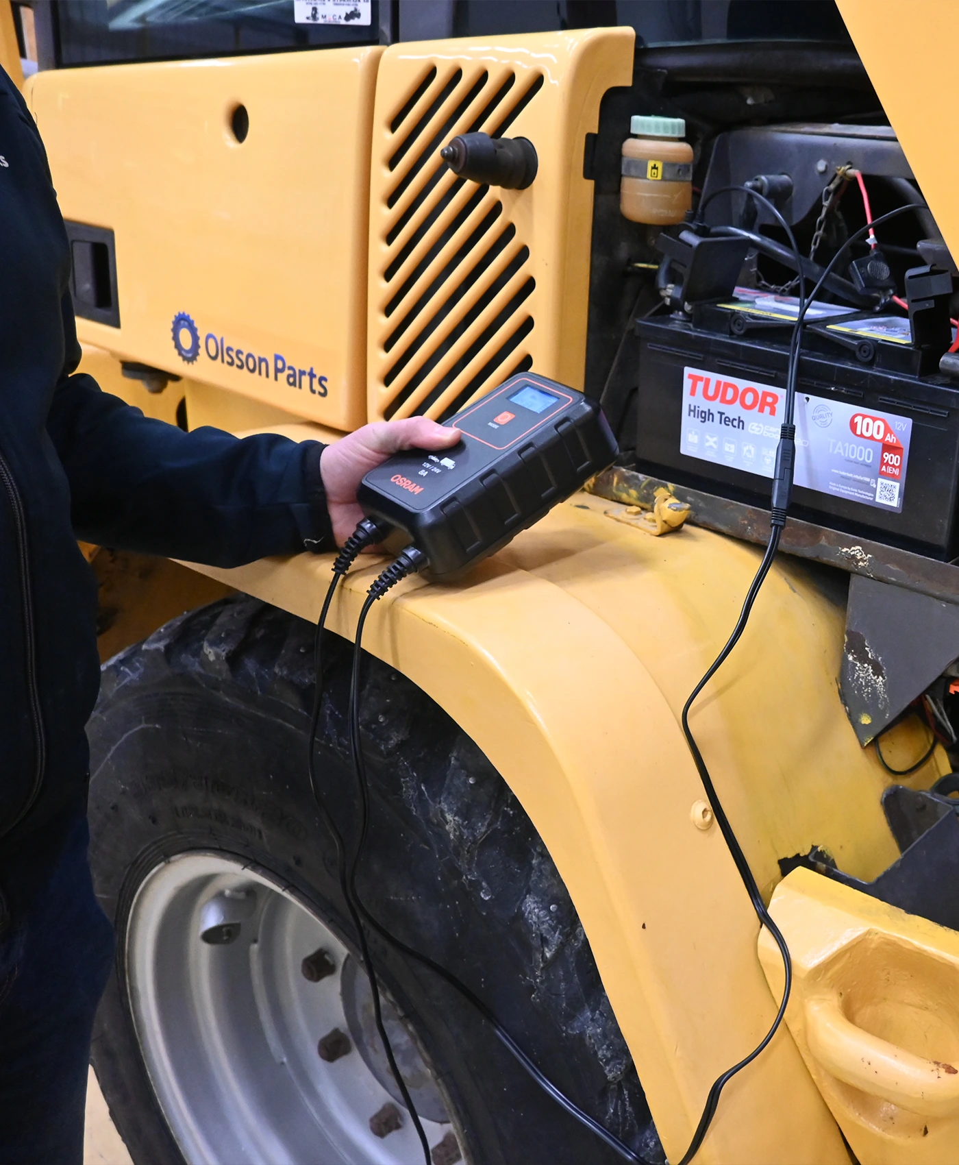 En tekniker anv&auml;nder en Osram-batteriladdare ansluten till ett Tudor High Tech-batteri monterat i en Volvo entreprenadmaskin.