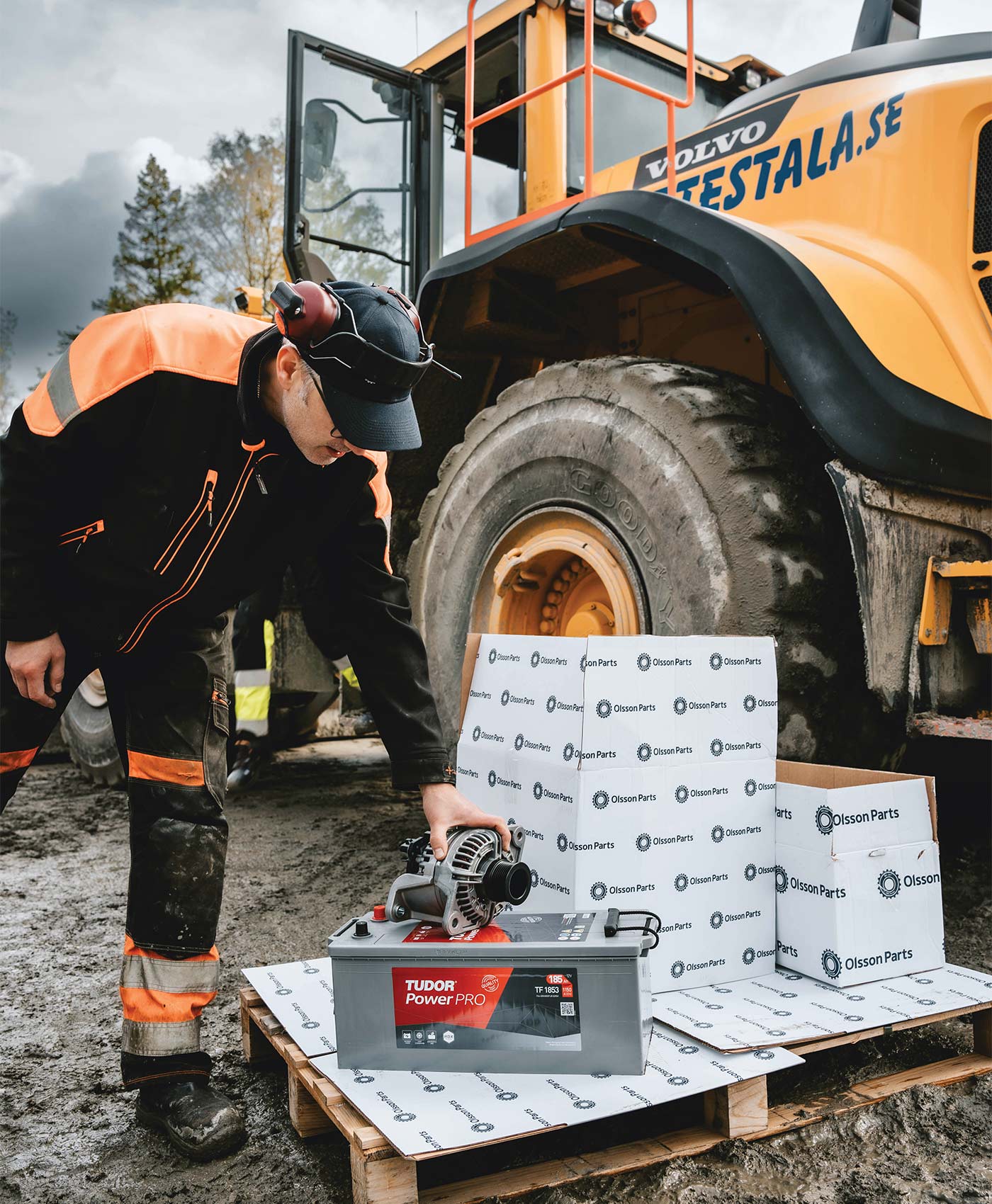 En person plockar upp en generator från en lastpall som ligger bredvid en Volvo hjullastare.