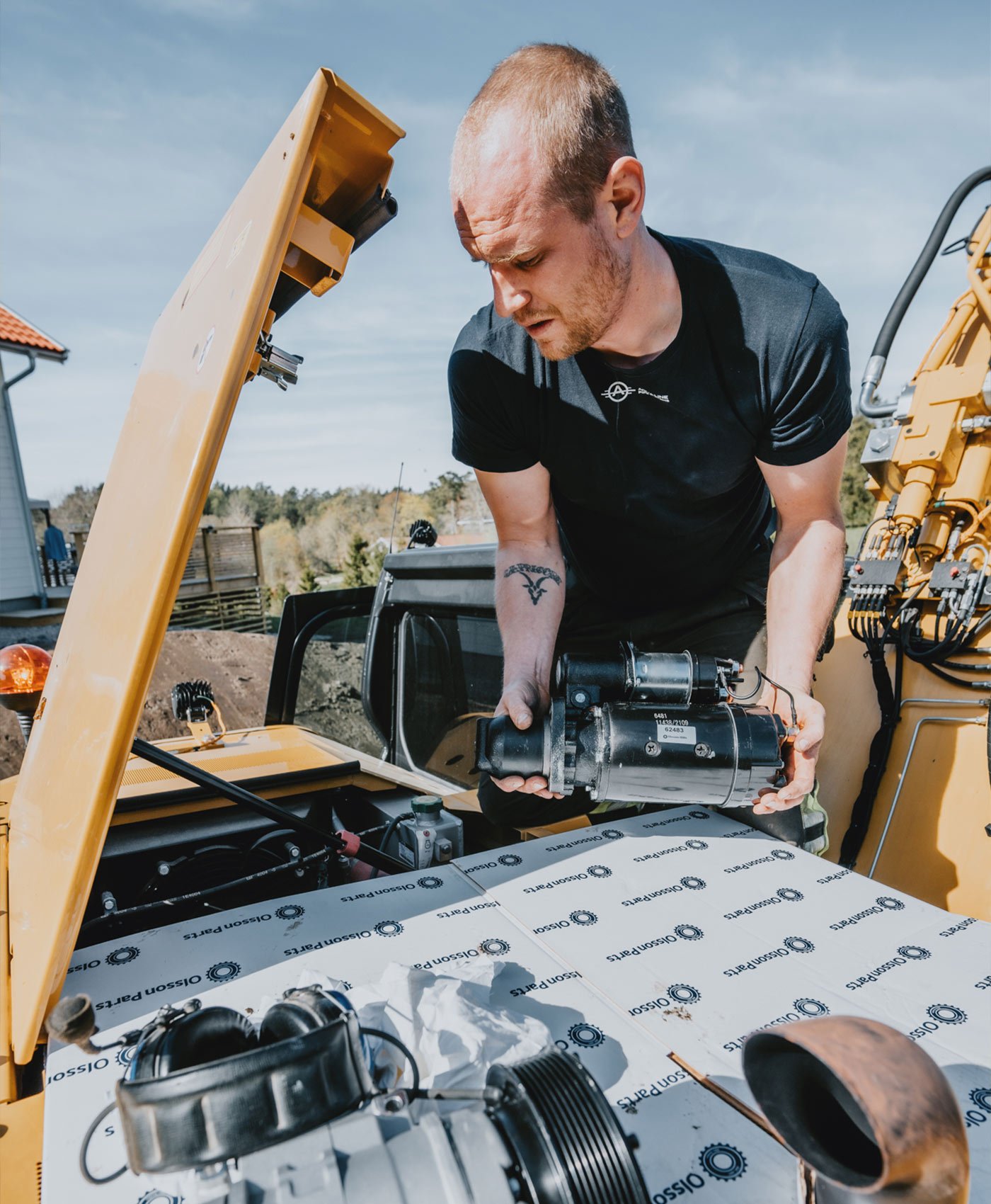 En person monterar en startmotor i ett öppet motorutrymme på en Caterpillar grävmaskin.