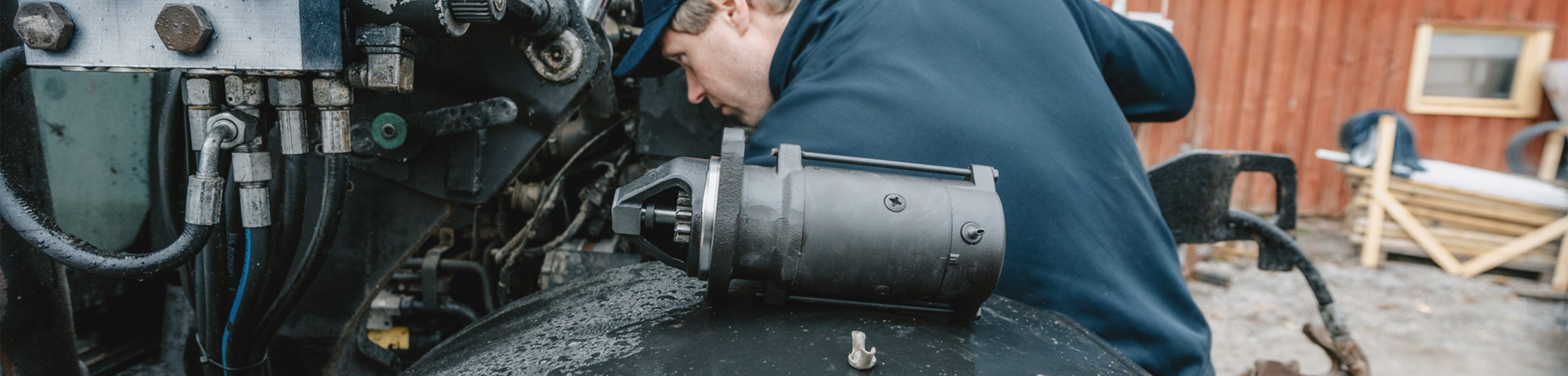 En person arbetar vid motorutrymmet på en traktor med en startmotor placerad bredvid.