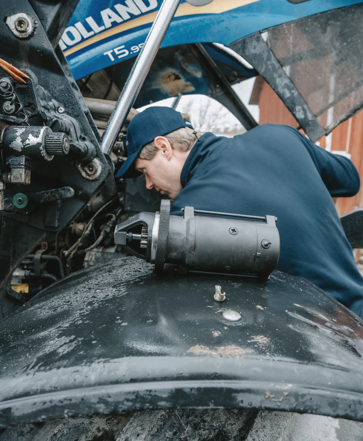 En person arbetar vid motorutrymmet p&aring; en traktor med en startmotor placerad bredvid.