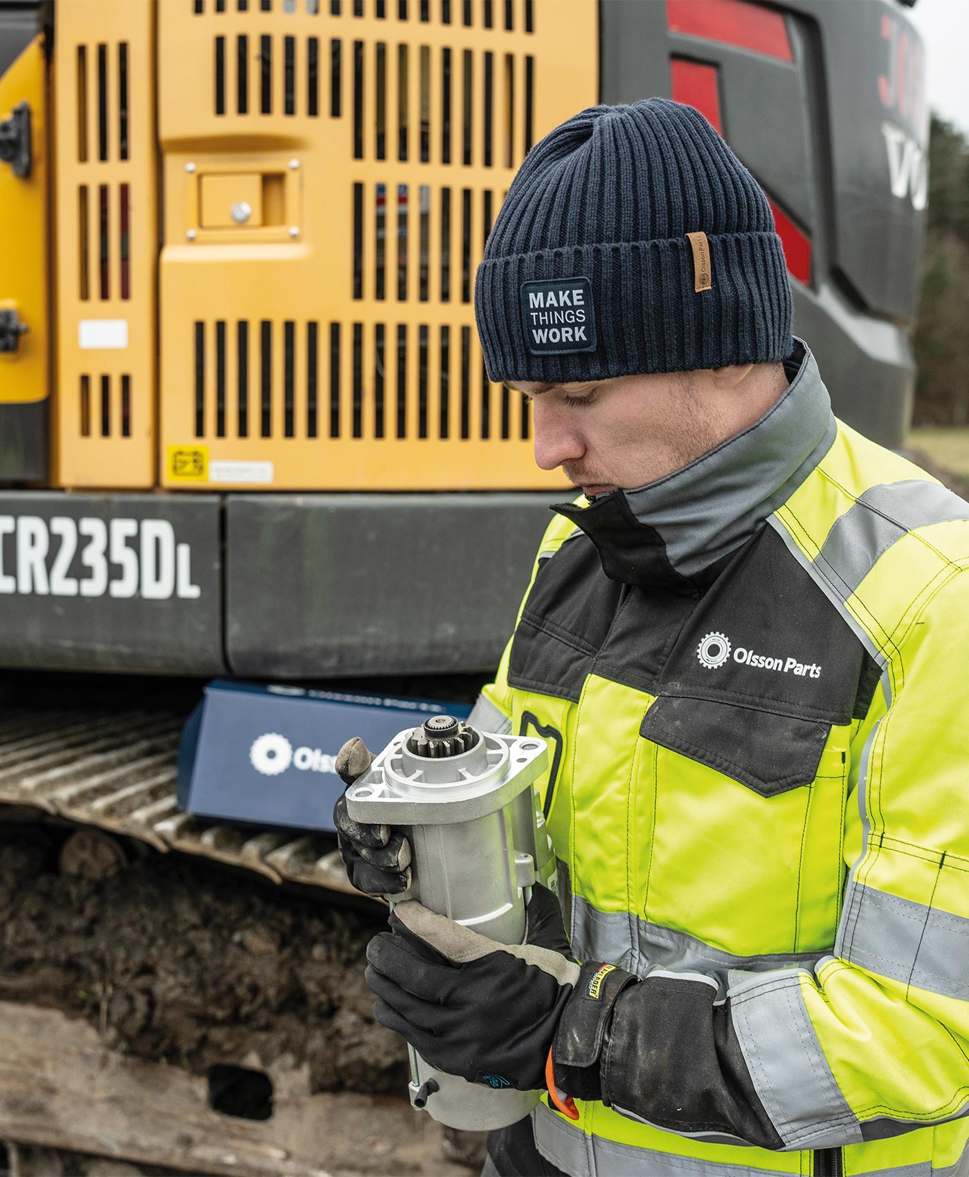 En person håller i en startmotor framför en Volvo grävmaskin.