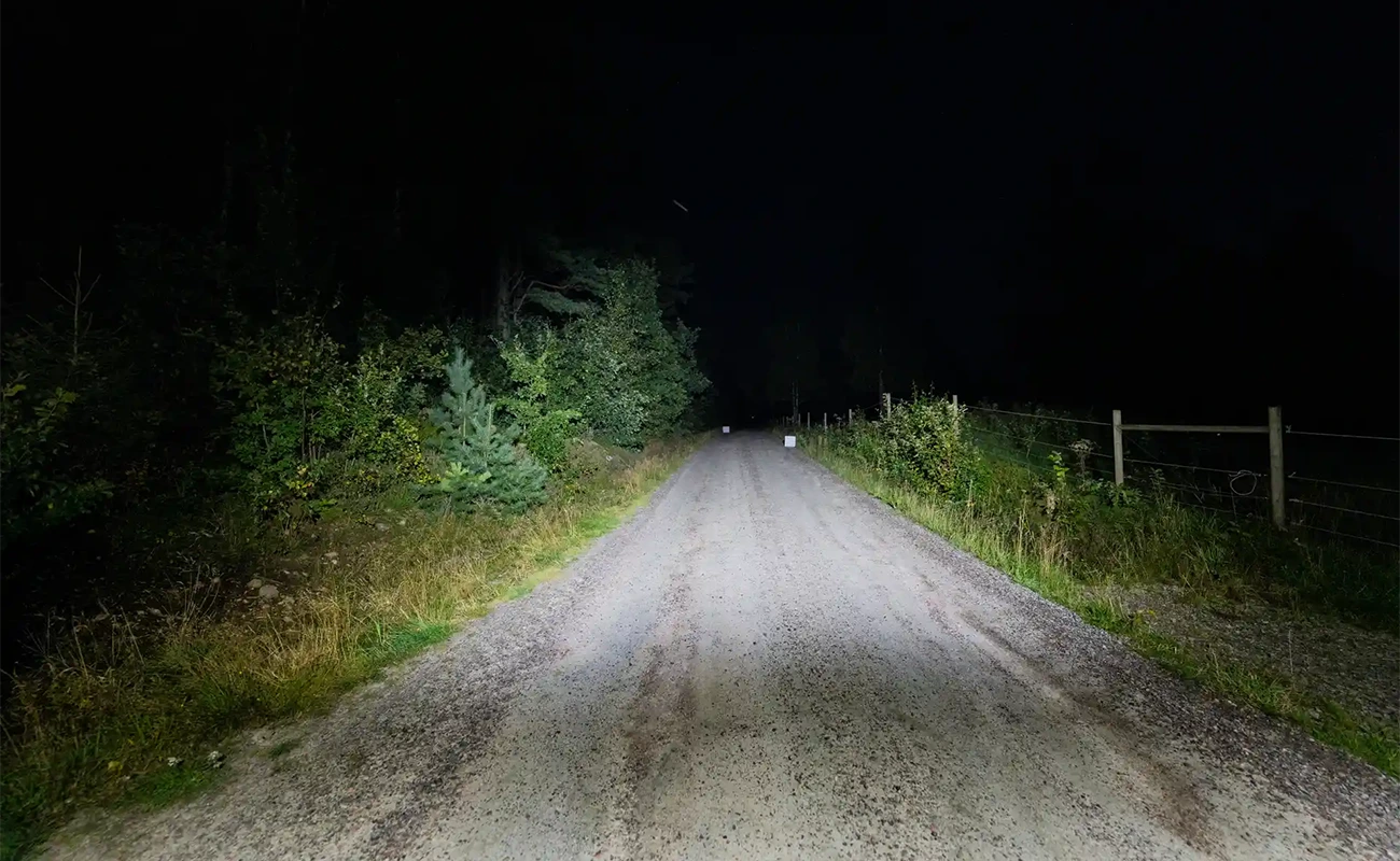 En upplyst grusv&auml;g en m&ouml;rk kv&auml;ll.