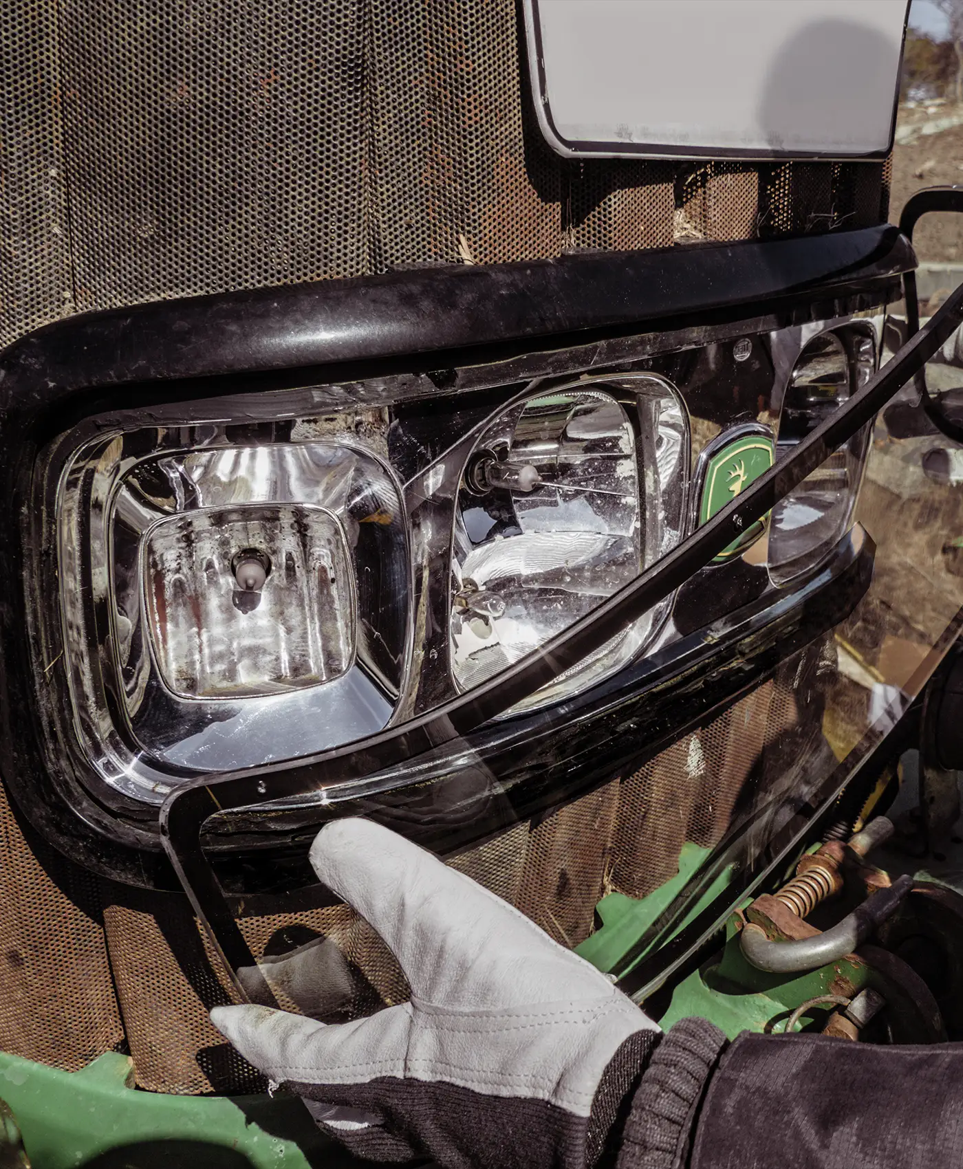 En person monterar glas p&aring; str&aring;lkastaren p&aring; en John Deere-traktor.