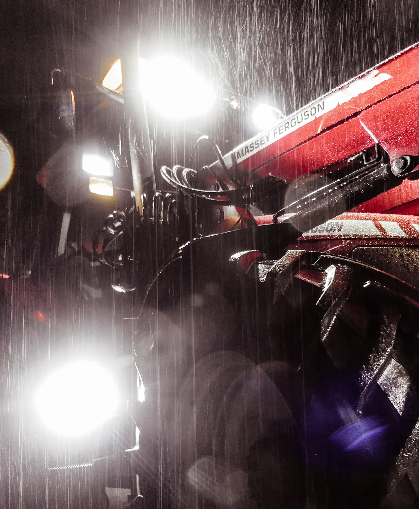 En Massey Ferguson-traktor med lampor som lyser upp regn.
