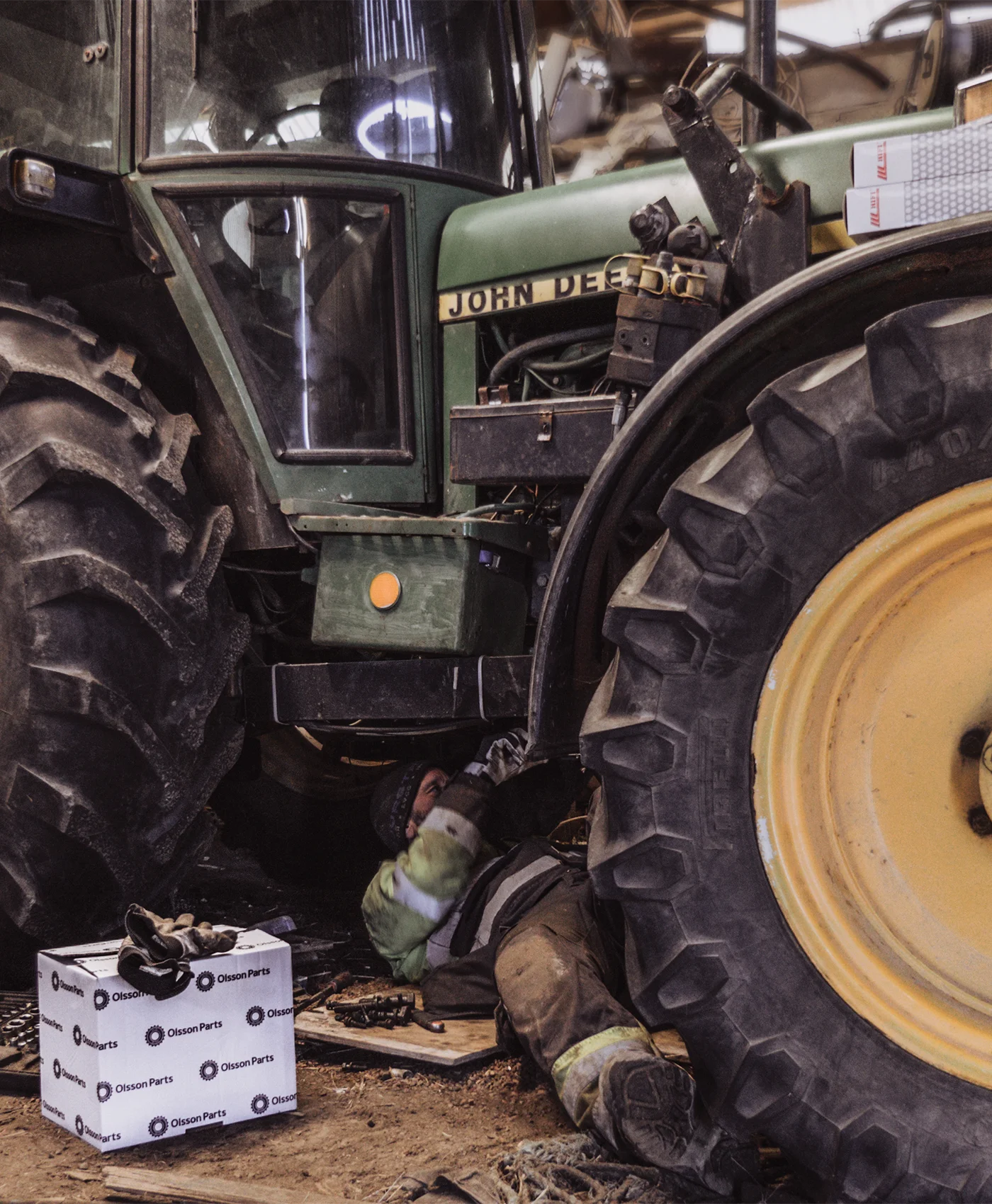 En person reparerer under en John Deere-traktor.