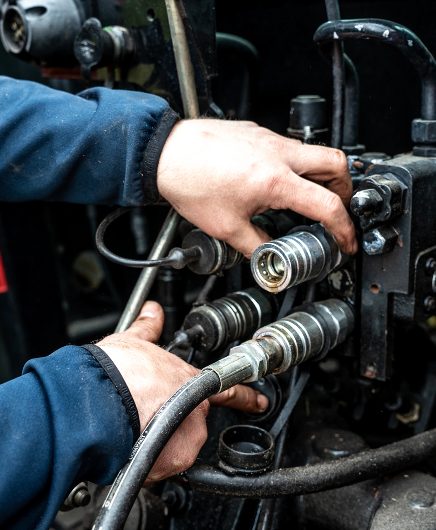 En person monterer hydraulikslanger med koblinger p&aring; en traktor.