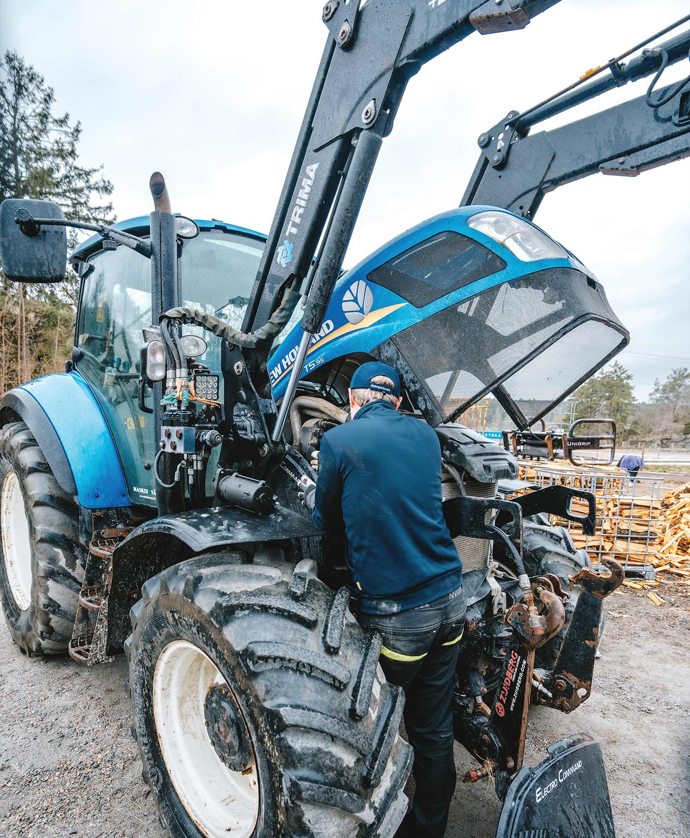 En person står och mekar under motorhuven på en New Holland-traktor.