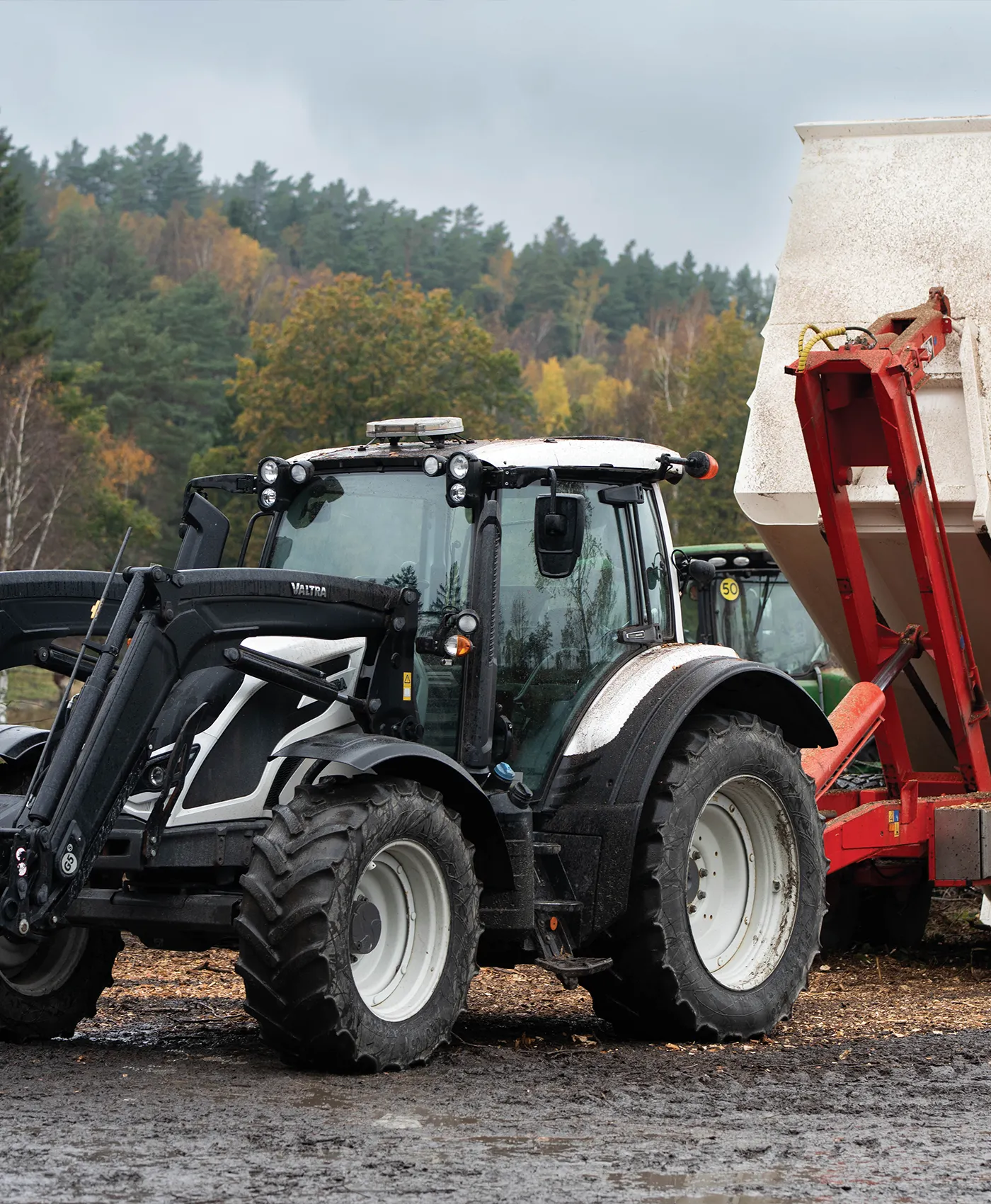 En Valtra-traktor med k&auml;rra st&aring;r parkerad framf&ouml;r en skog.