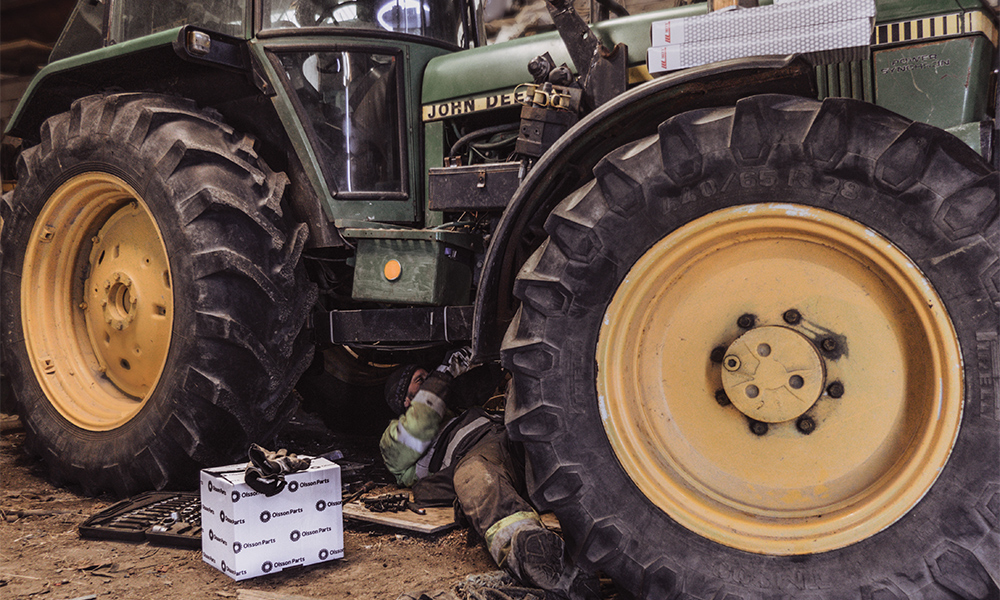 A man working under a green John Deere tractor.