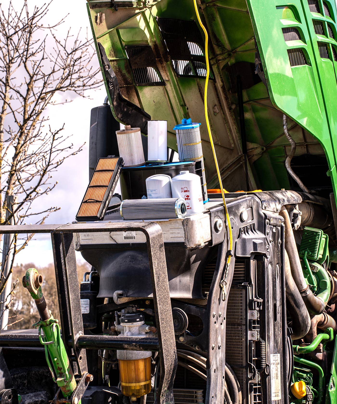 Green John Deere tractor with its hood open with several filters placed on the engine.