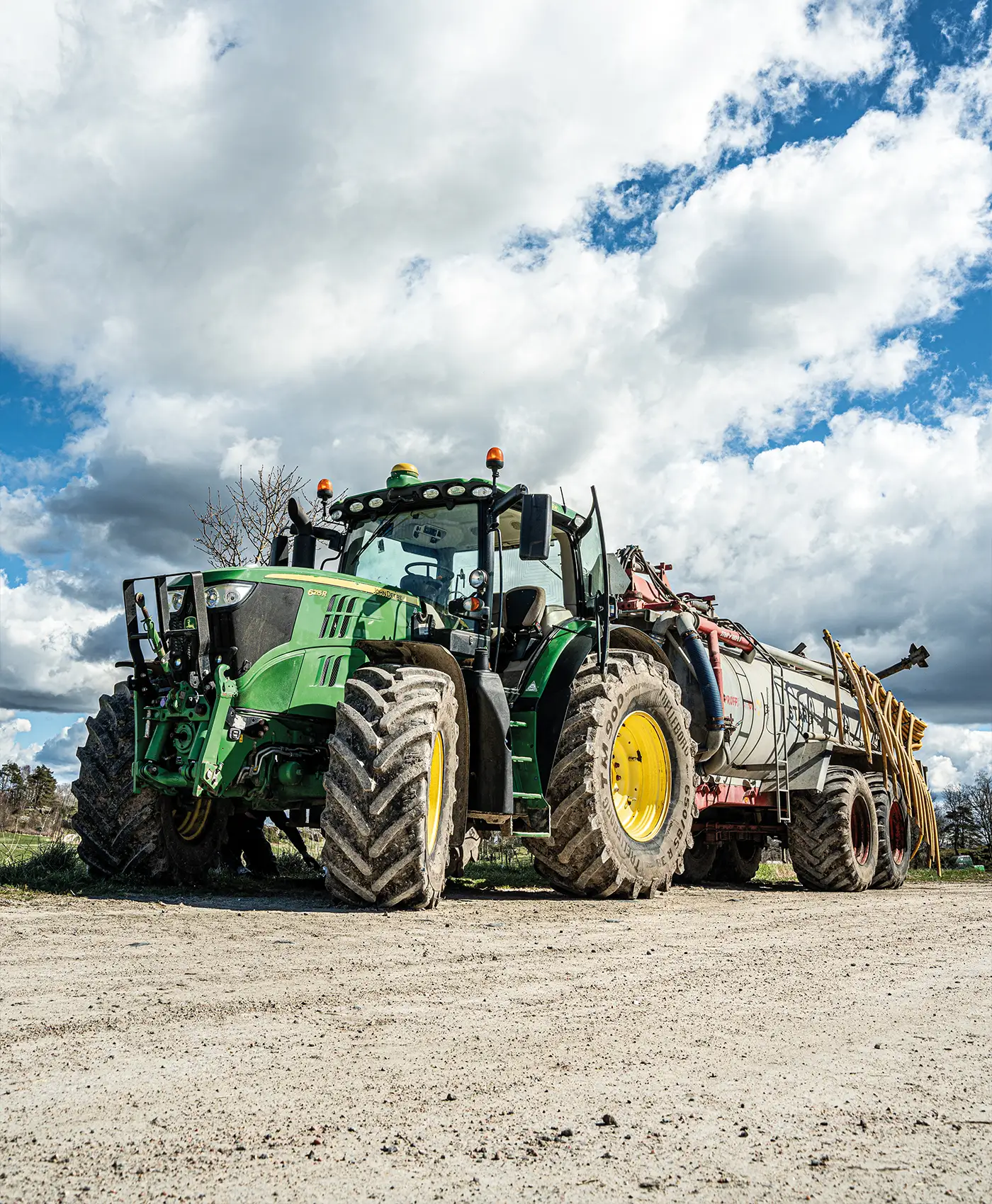En gr&ouml;n John Deere traktor med en g&ouml;dselspridare bakom.