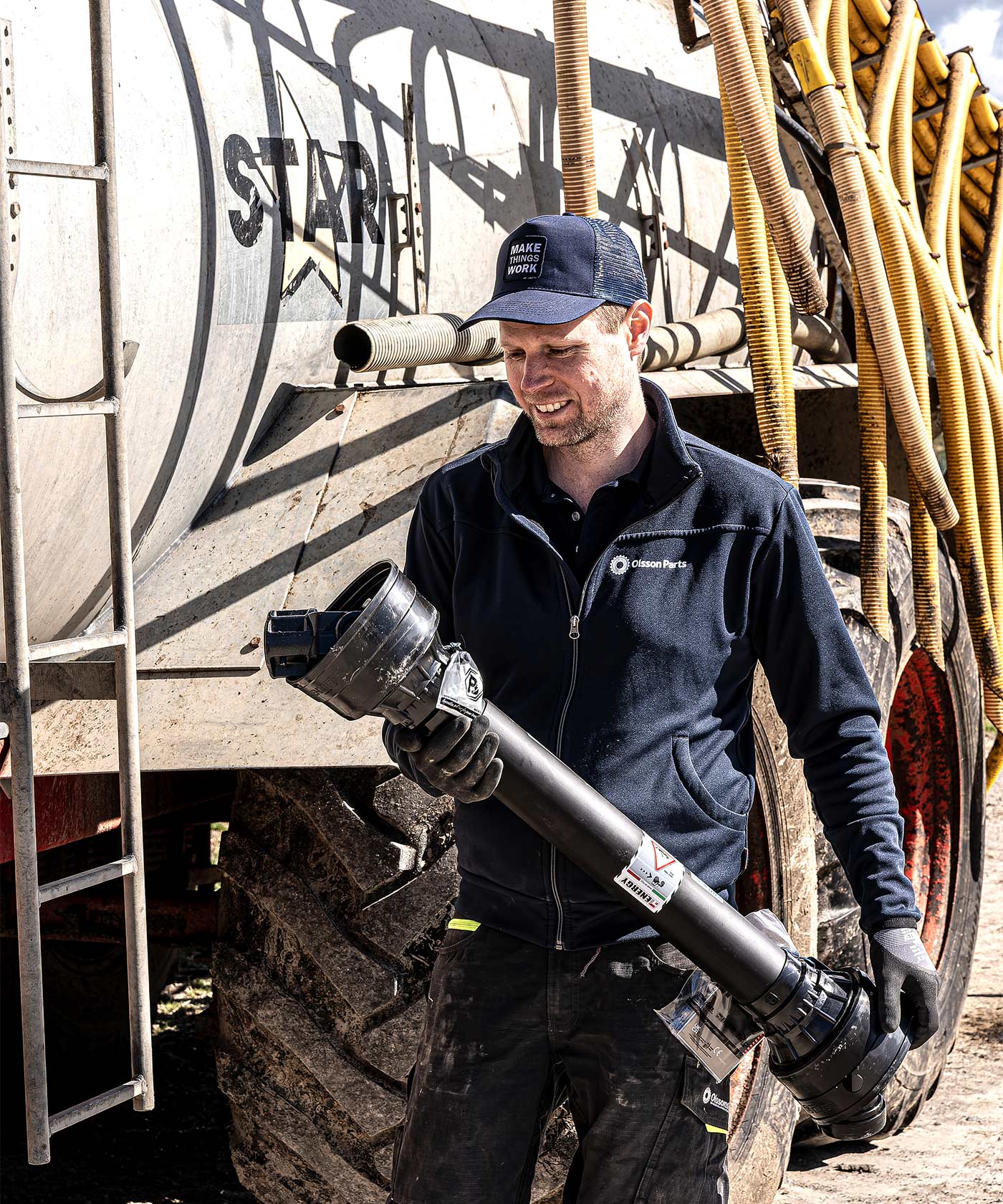 A man holding a PTO shaft and walking in front of a fertiliser spreader.