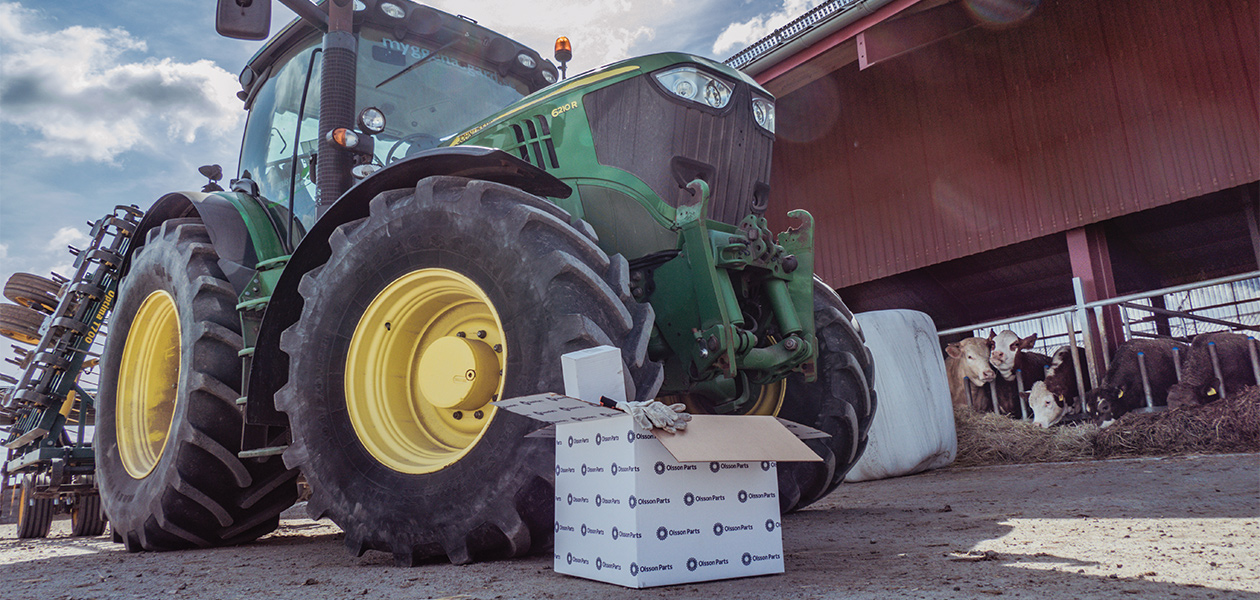 A green John Deere in front of a barn with cows. In front of the tractor is an Olsson Parts box