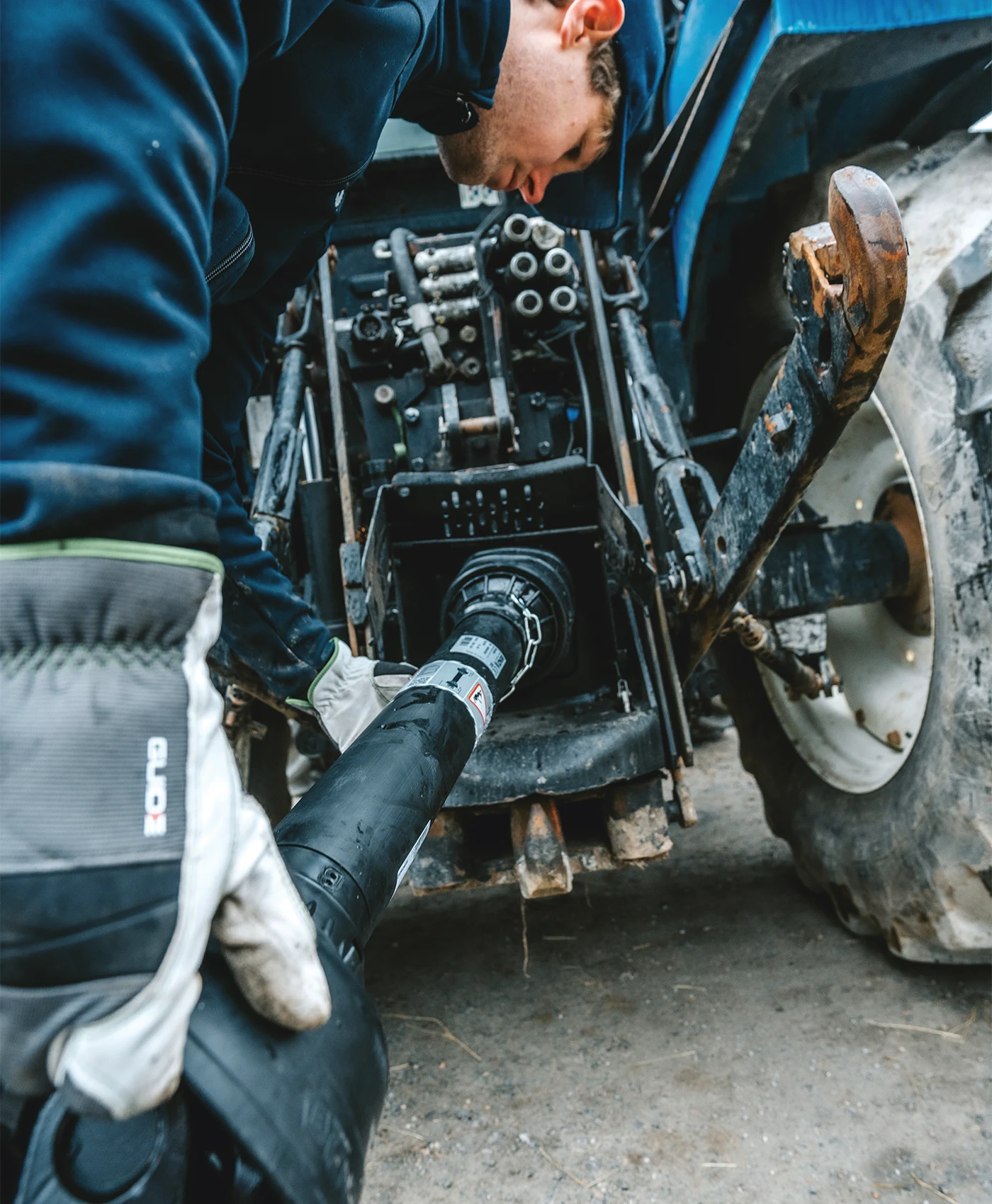 En person monterar en kraft&ouml;verf&ouml;ringsaxel p&aring; en New Holland traktor.
