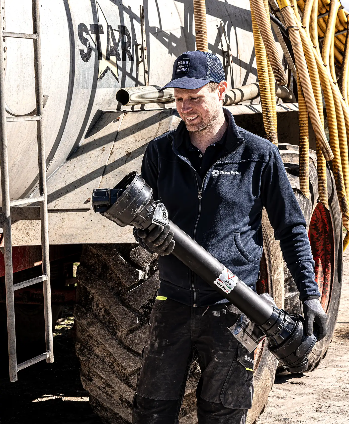 En person g&aring;r bredvid en g&ouml;dselspridare b&auml;randes p&aring; en kraft&ouml;verf&ouml;ringsaxel.