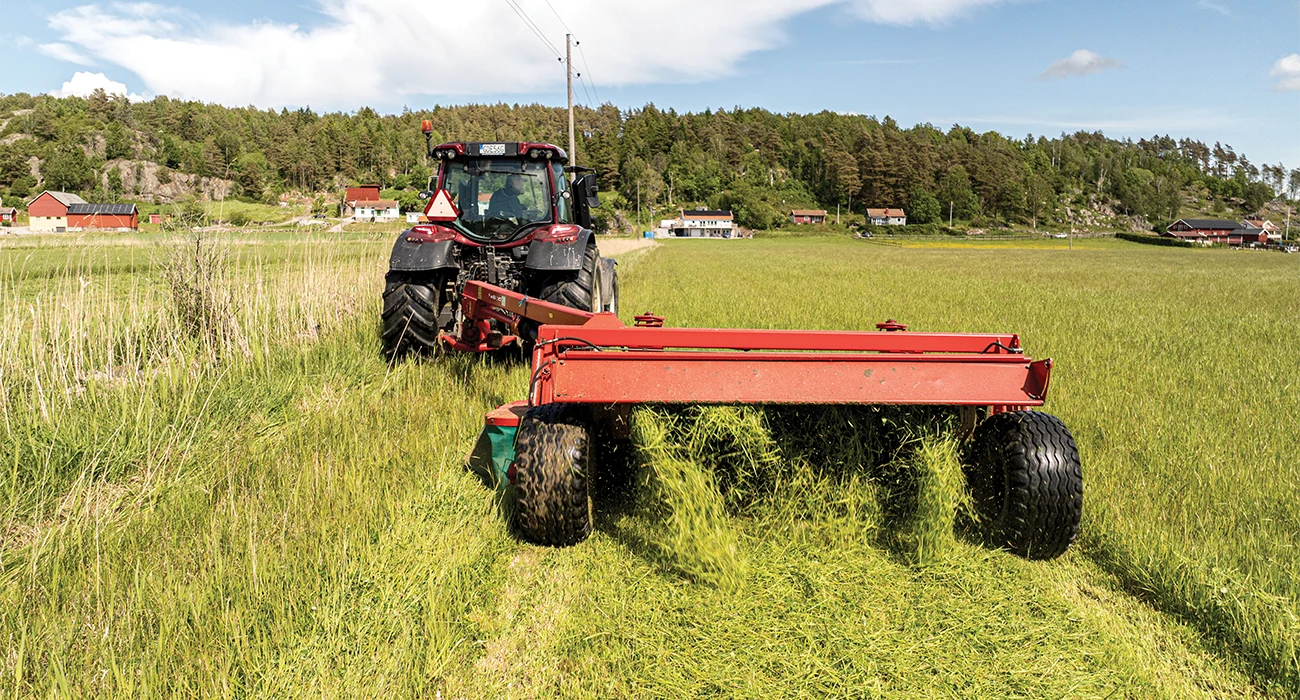 En Valtra traktor sl&aring;r gr&auml;s p&aring; ett gr&ouml;nt f&auml;lt.