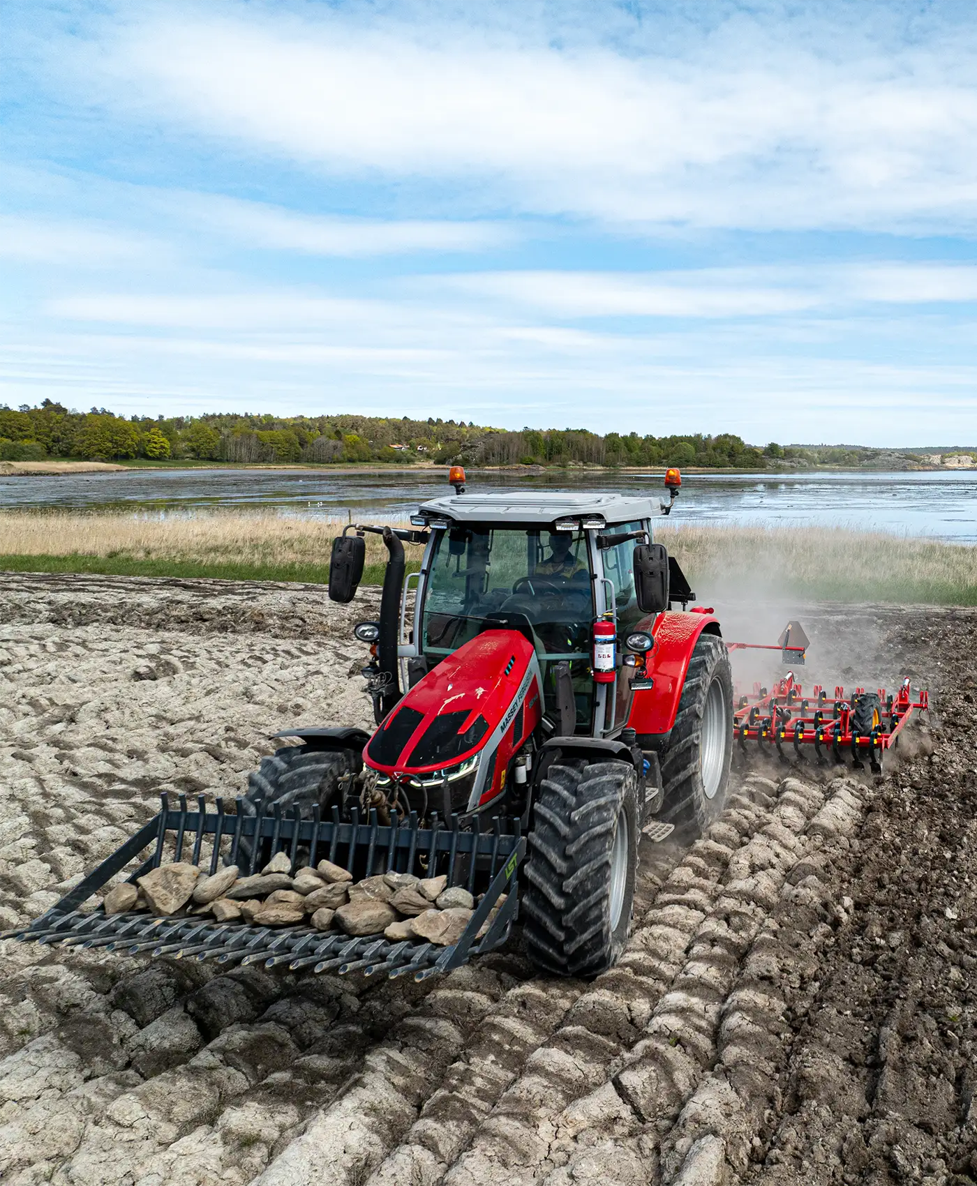 Ein Massey Ferguson Traktor fährt über ein Feld und zieht eine Egge, mit einem vorne montierten Steinsammler