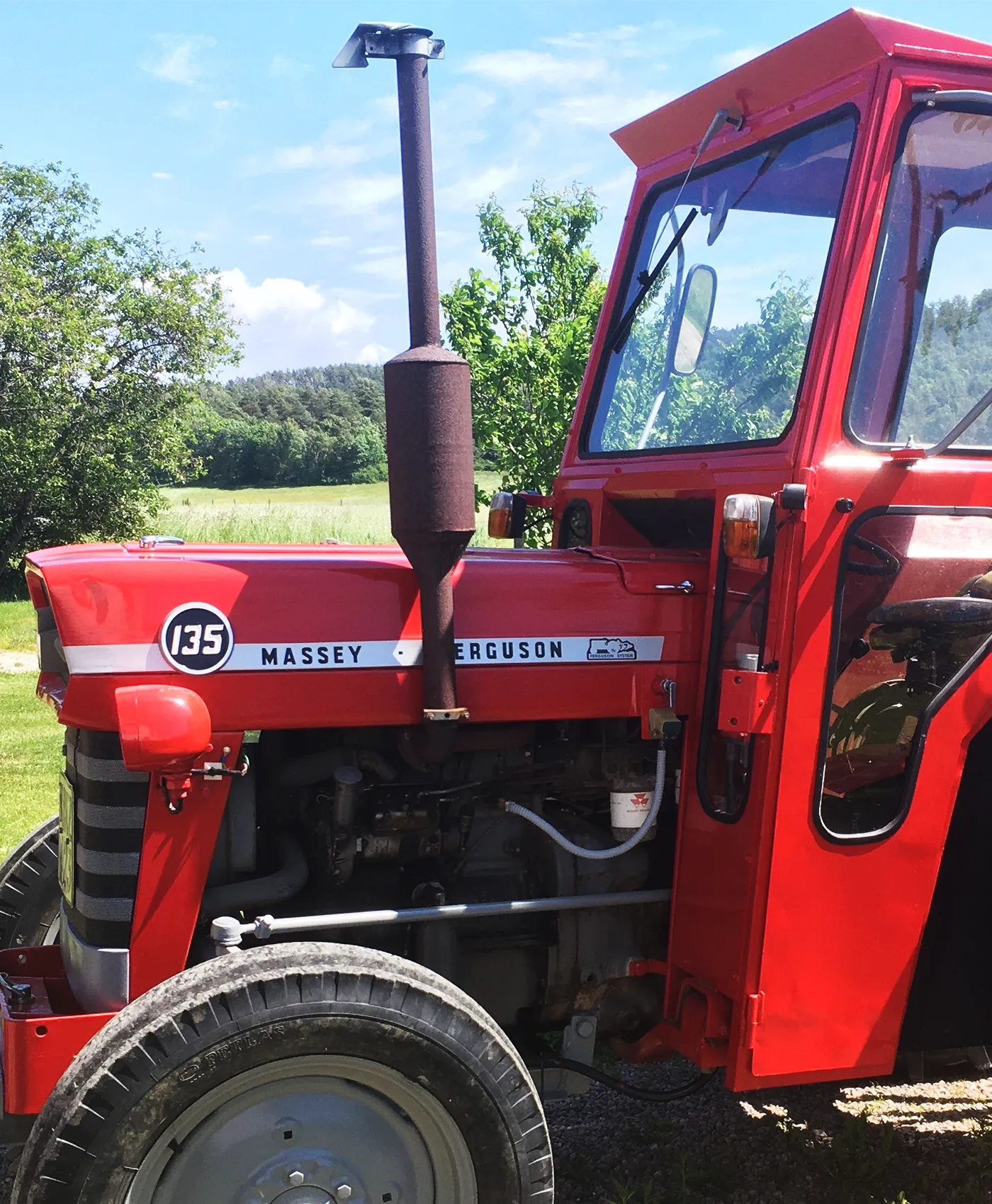 En Massey Ferguson 135 står parkeret foran en skov.