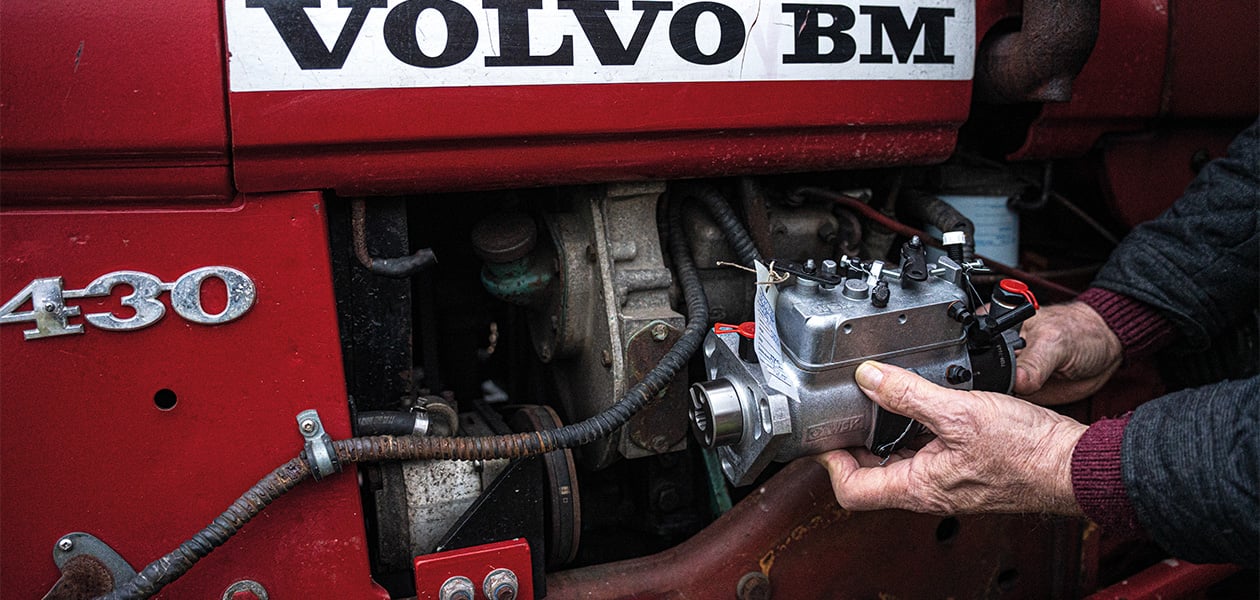 En person som håller i en reservdel framför en röd Volvo BM-traktor.