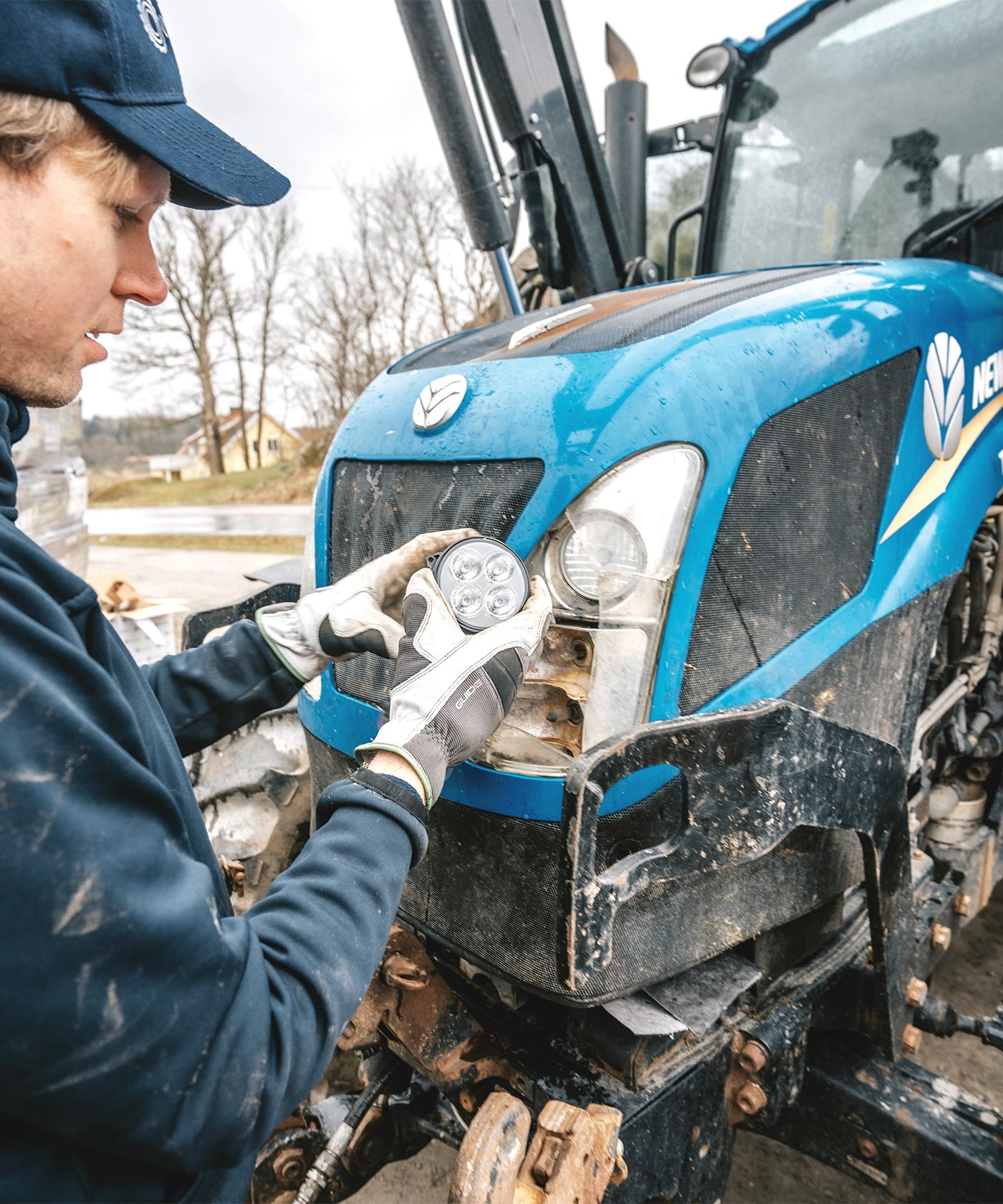 En person som håller en strålkastare framför huven på en blå traktor.