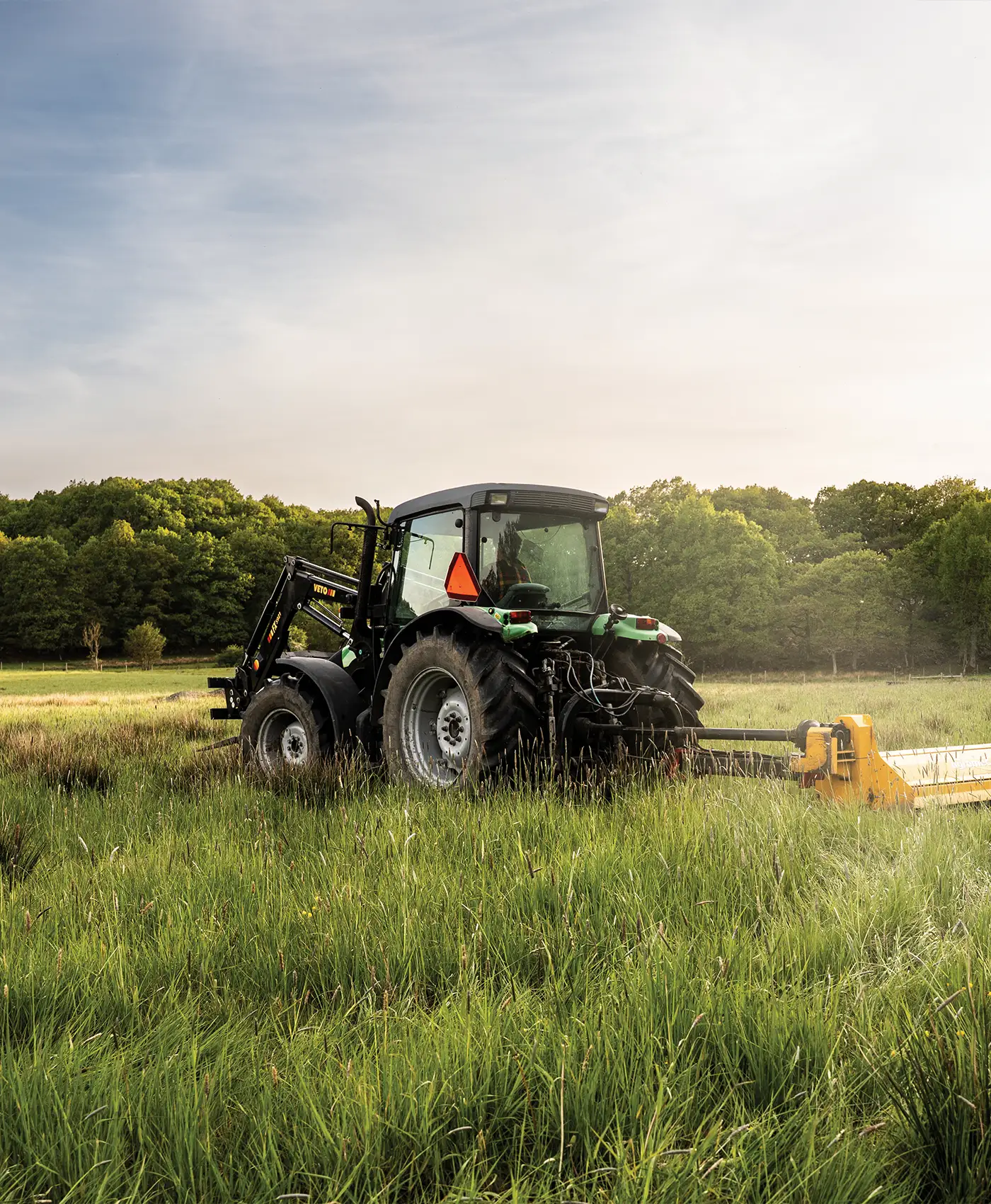 En gr&oslash;n traktor st&aring;r p&aring; en mark med en sl&aring;maskine.