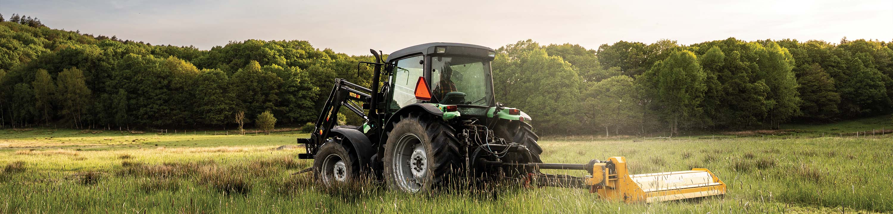 En grön traktor står på ett fält med en slåttermaskin.