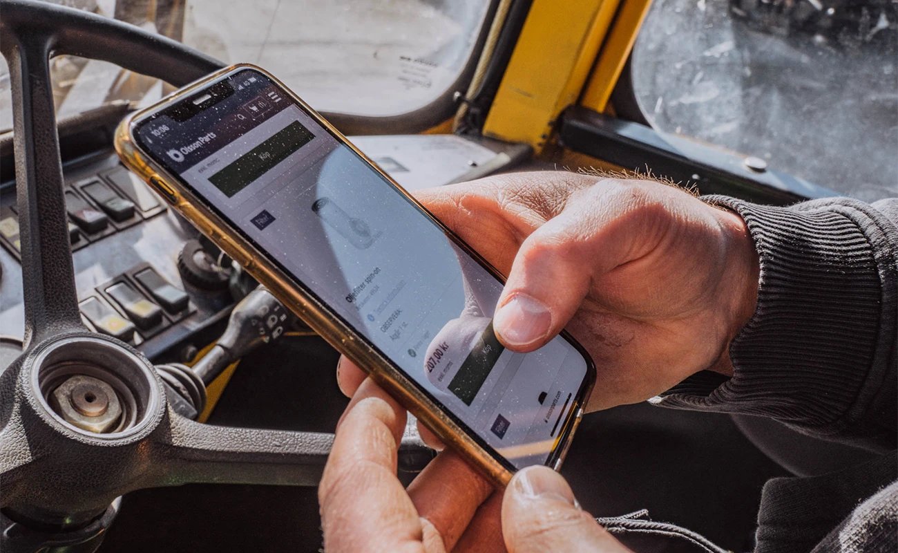 En person interagerar med Olsson Parts hemsida på en mobiltelefon i en maskinhytt.