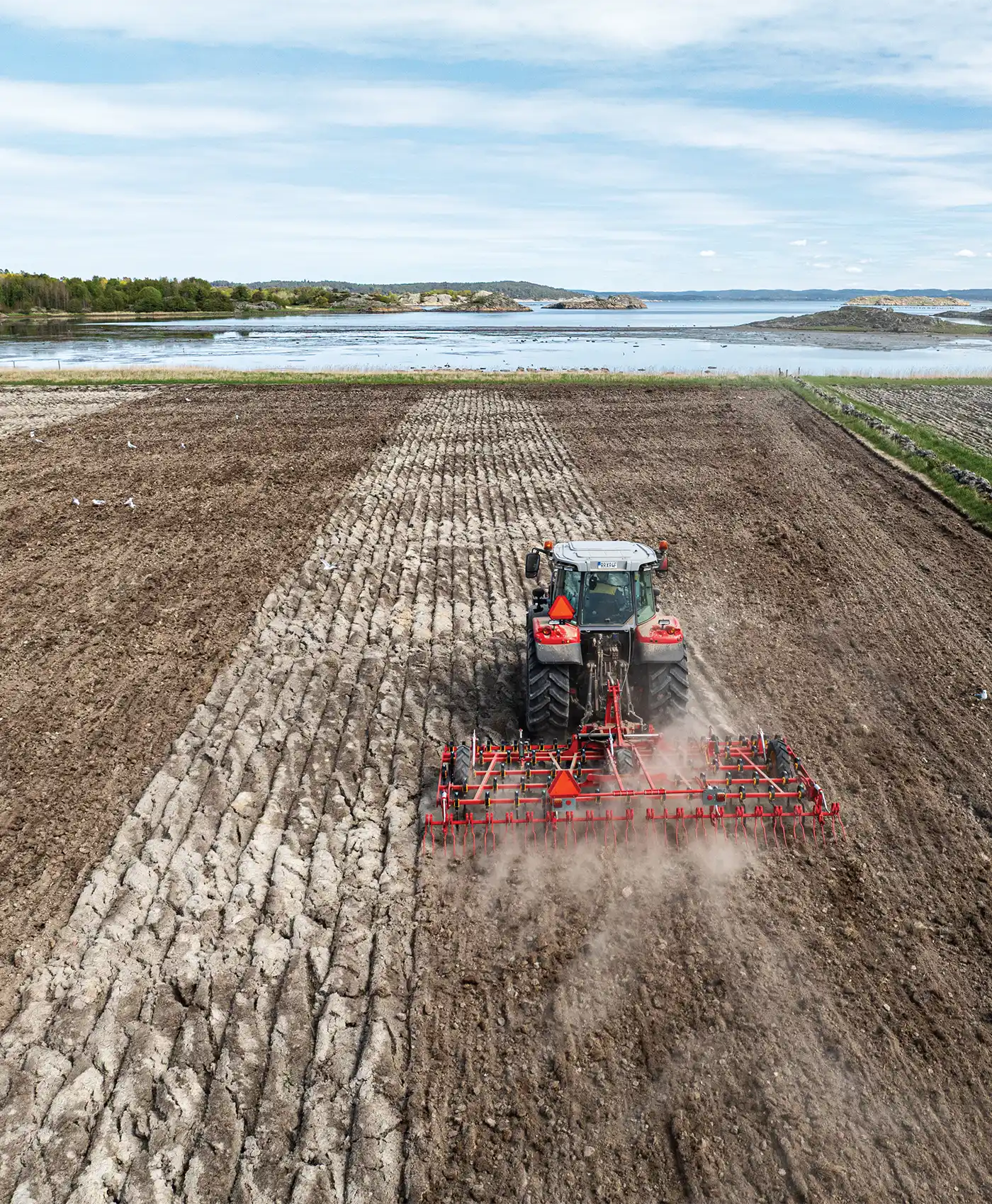 En Massey Ferguson traktor som harvar p&aring; ett f&auml;lt vid havet.