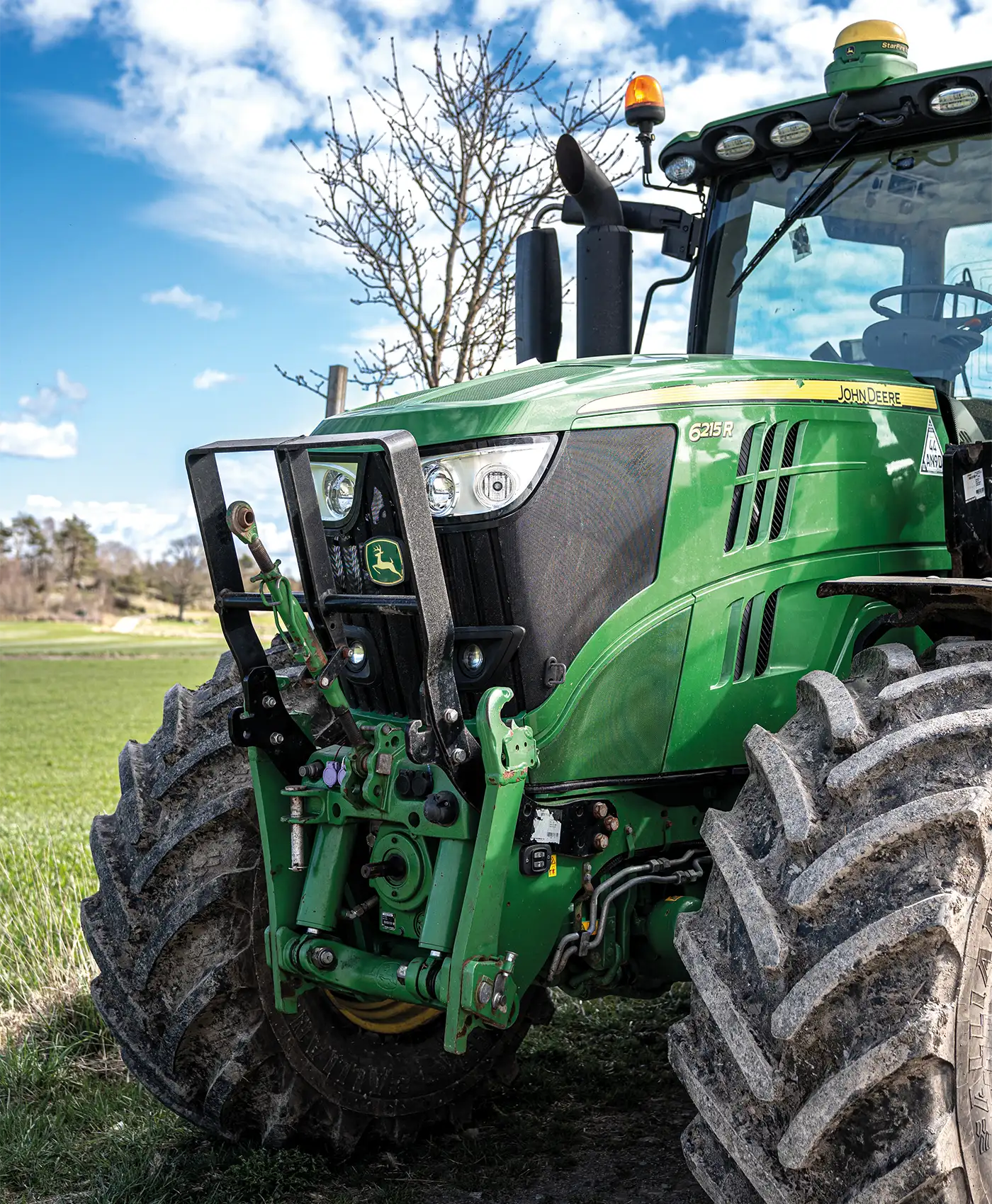 En John Deere traktor st&aring;r framf&ouml;r ett gr&ouml;nt f&auml;lt.