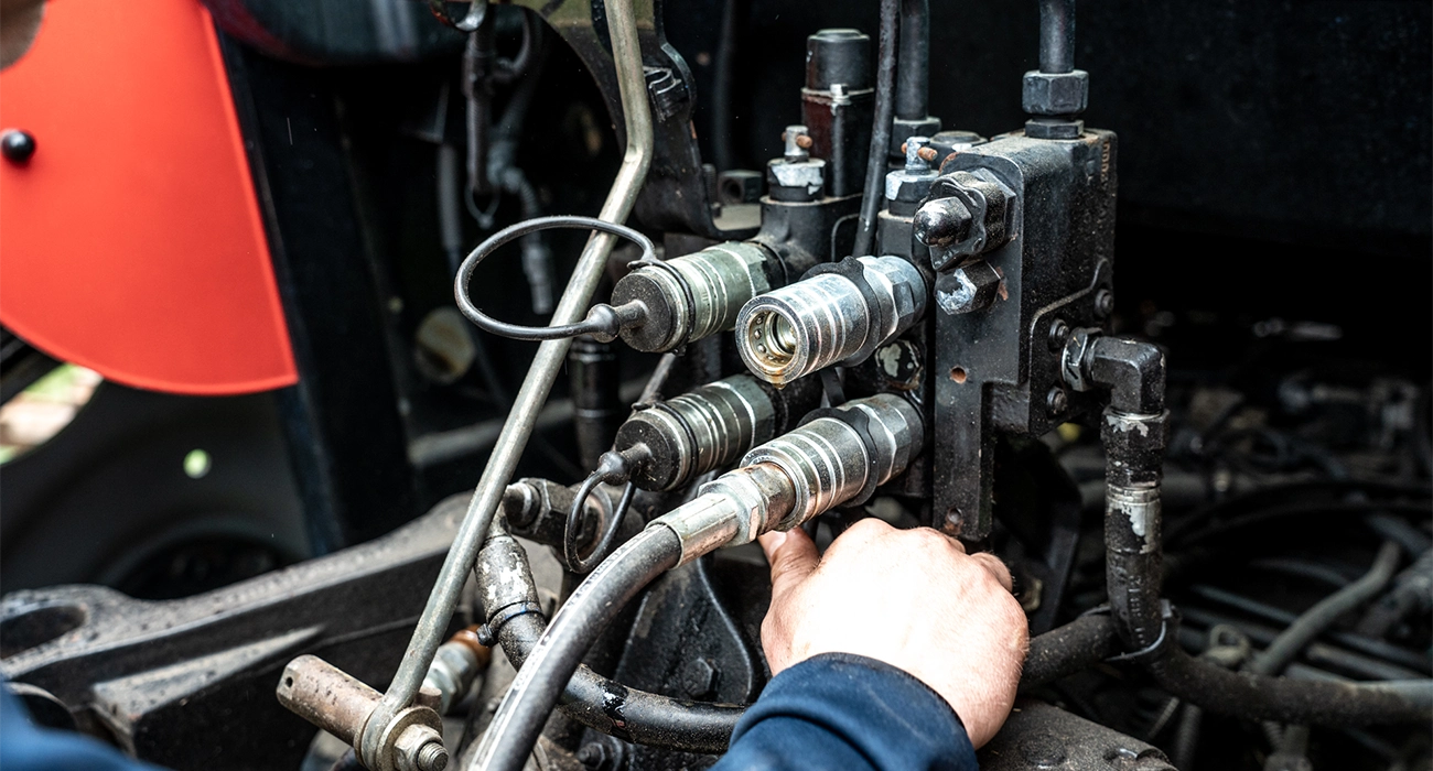 En person monterar hydraulslang i kopplingar på en traktor.