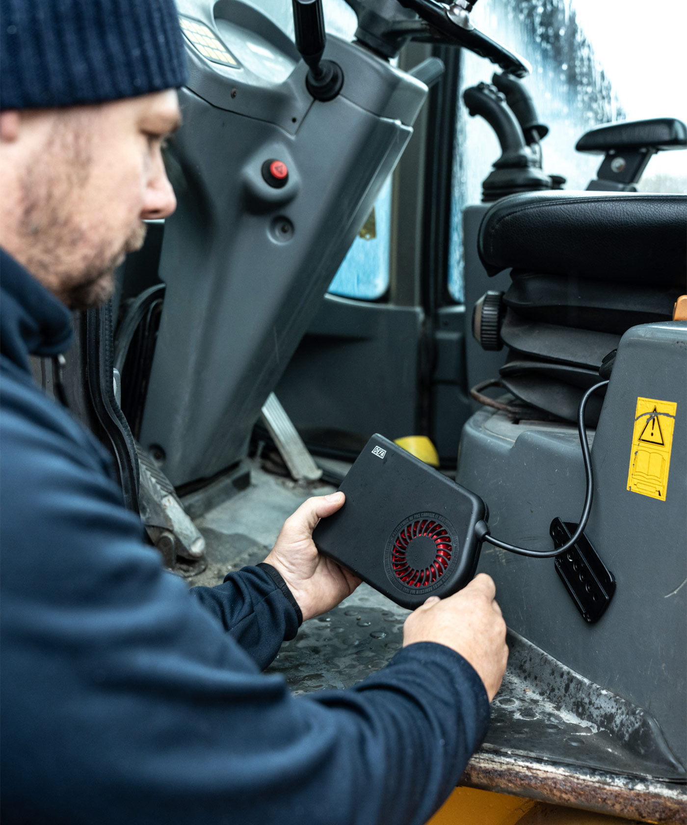 En person placerar en kupévärmare i hytten på en Volvo hjullastare.