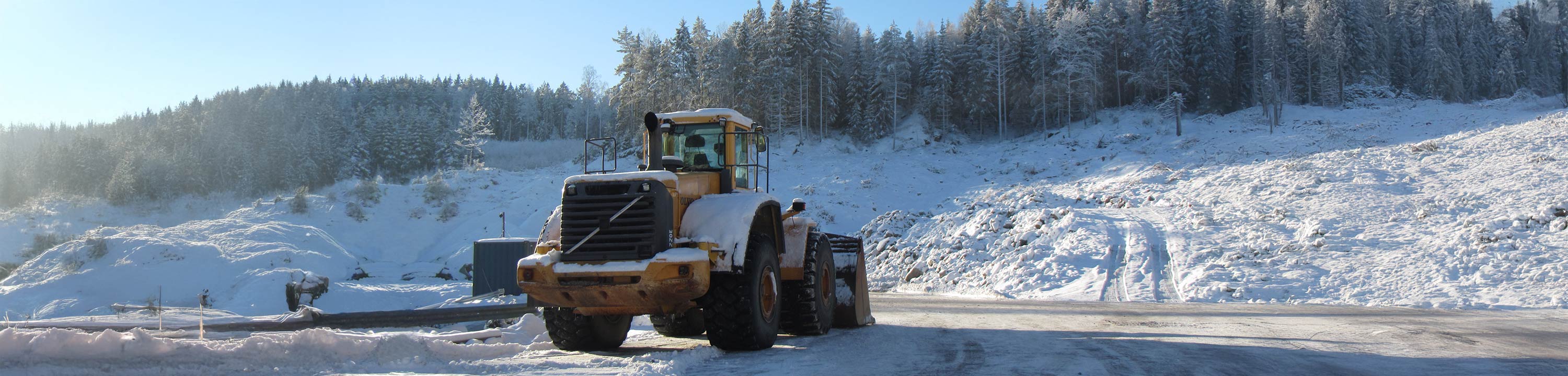 En snötäckt Volvo-hjullastare står parkerad framför en skog.