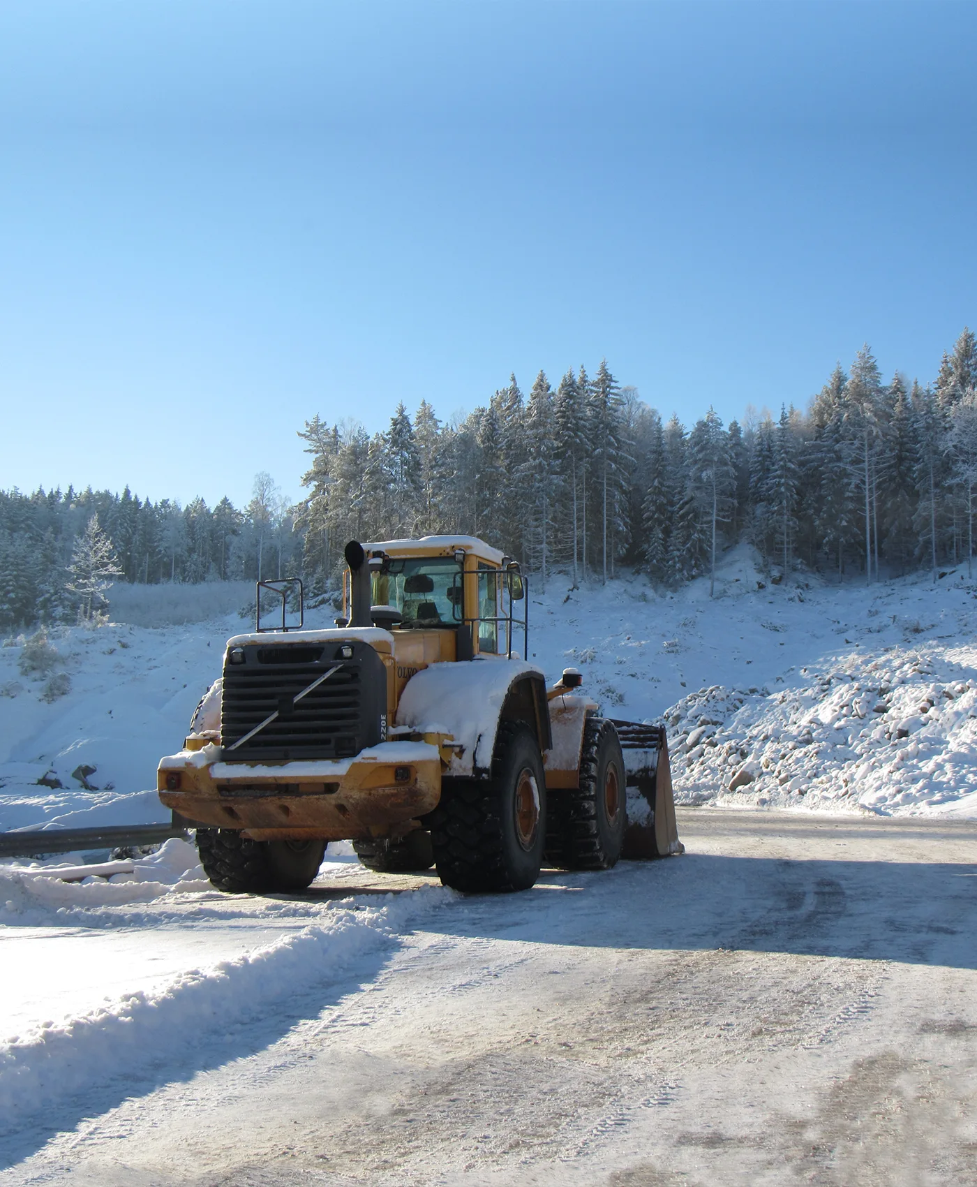 En sn&ouml;t&auml;ckt Volvo-hjullastare st&aring;r parkerad framf&ouml;r en skog.