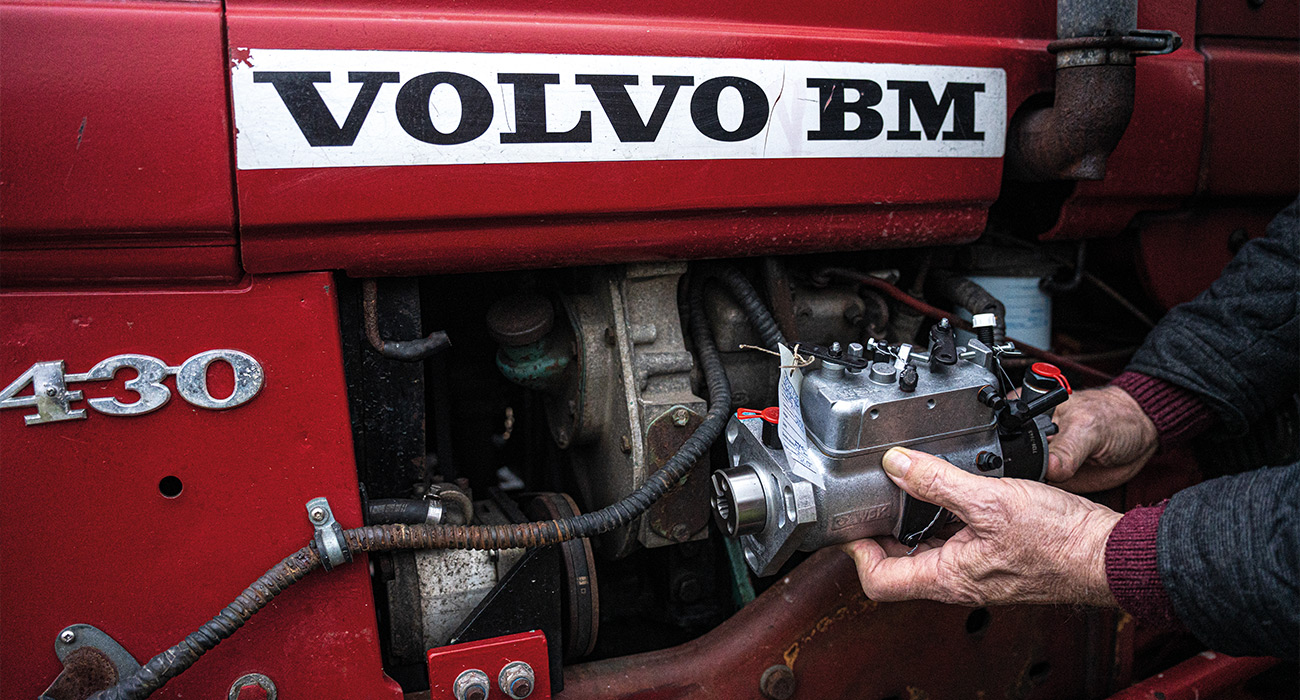 En person monterar en pump på motorn i en röd Volvo BM 430-traktor.