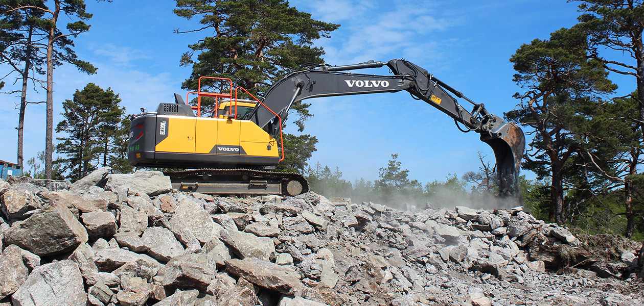 En Volvo-gravemaskin som står på en haug med stein og graver