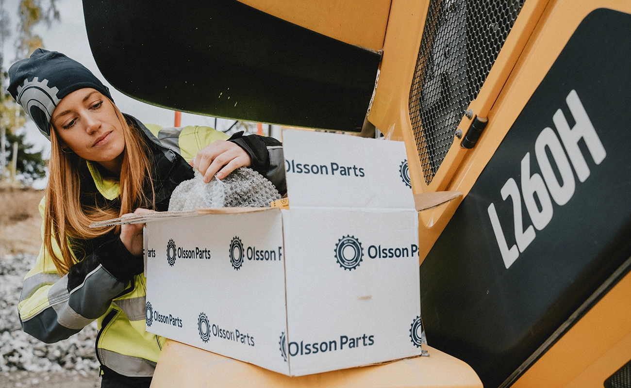 En person pakker varer ud fra en Olsson Parts-kasse ved en Volvo gummiged.