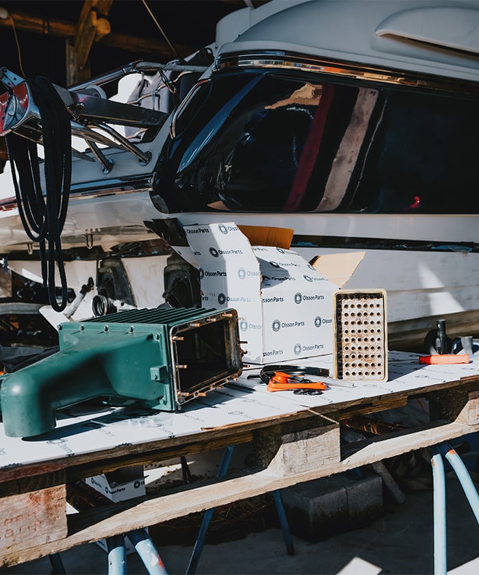 Spare parts and tools placed on a work table in front of a boat.