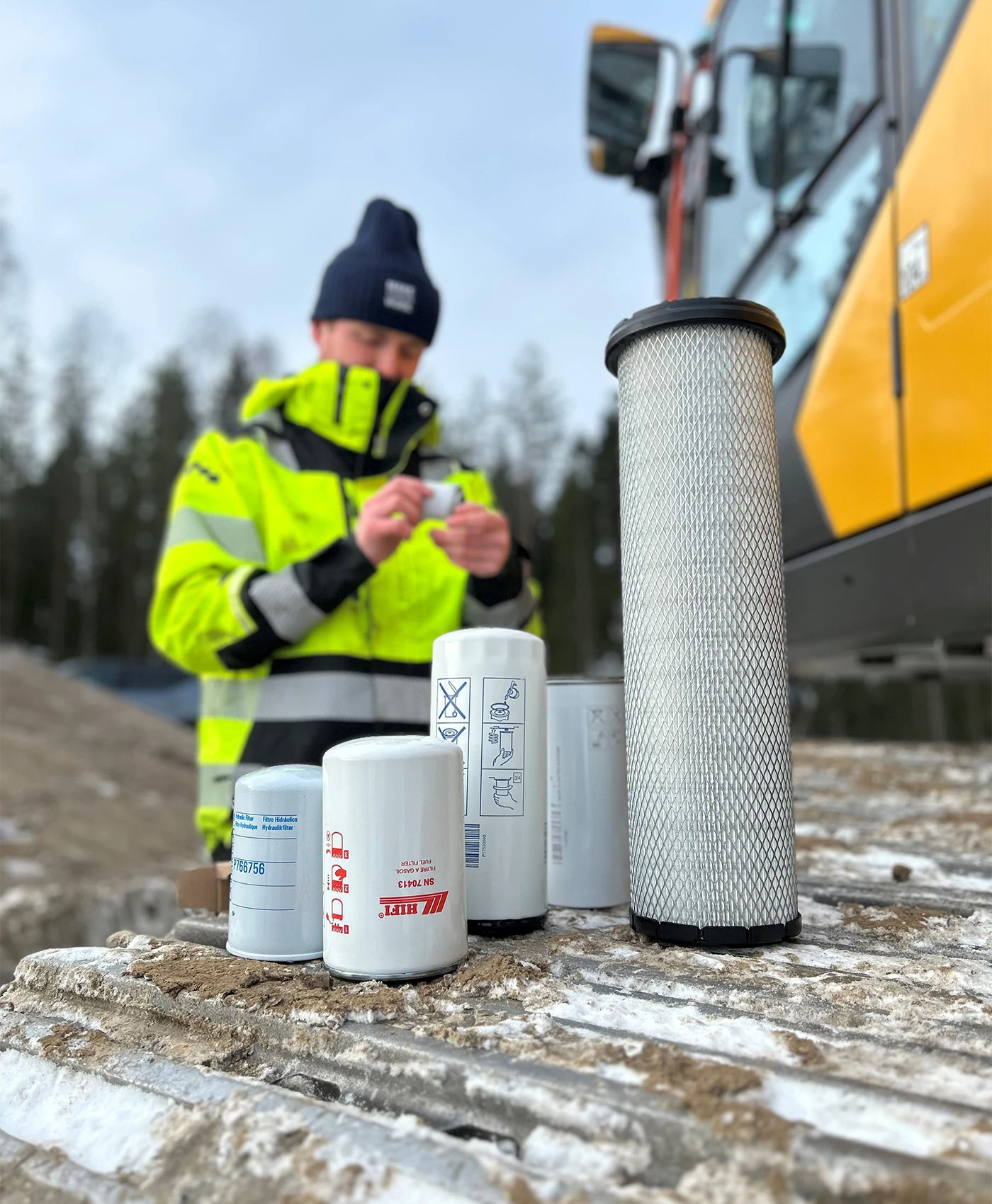 Forskellige filtre er placeret p&aring; larveb&aring;ndene p&aring; en Volvo gravemaskine. I baggrunden holder en person et filter.
