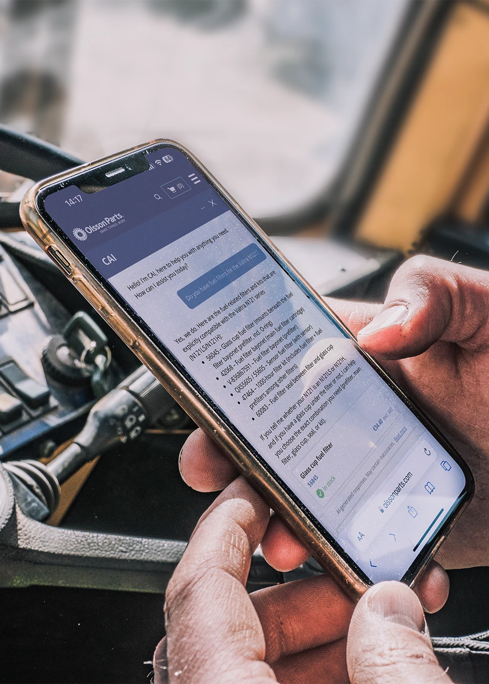 A person holding a mobile phone showing Olsson Parts&rsquo; chatbot CAI, used while working in a machine.