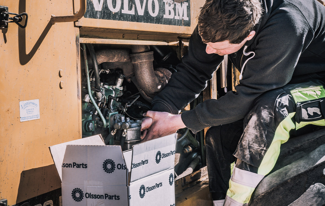 En man sitter och skruvar på en gul hjullastare.